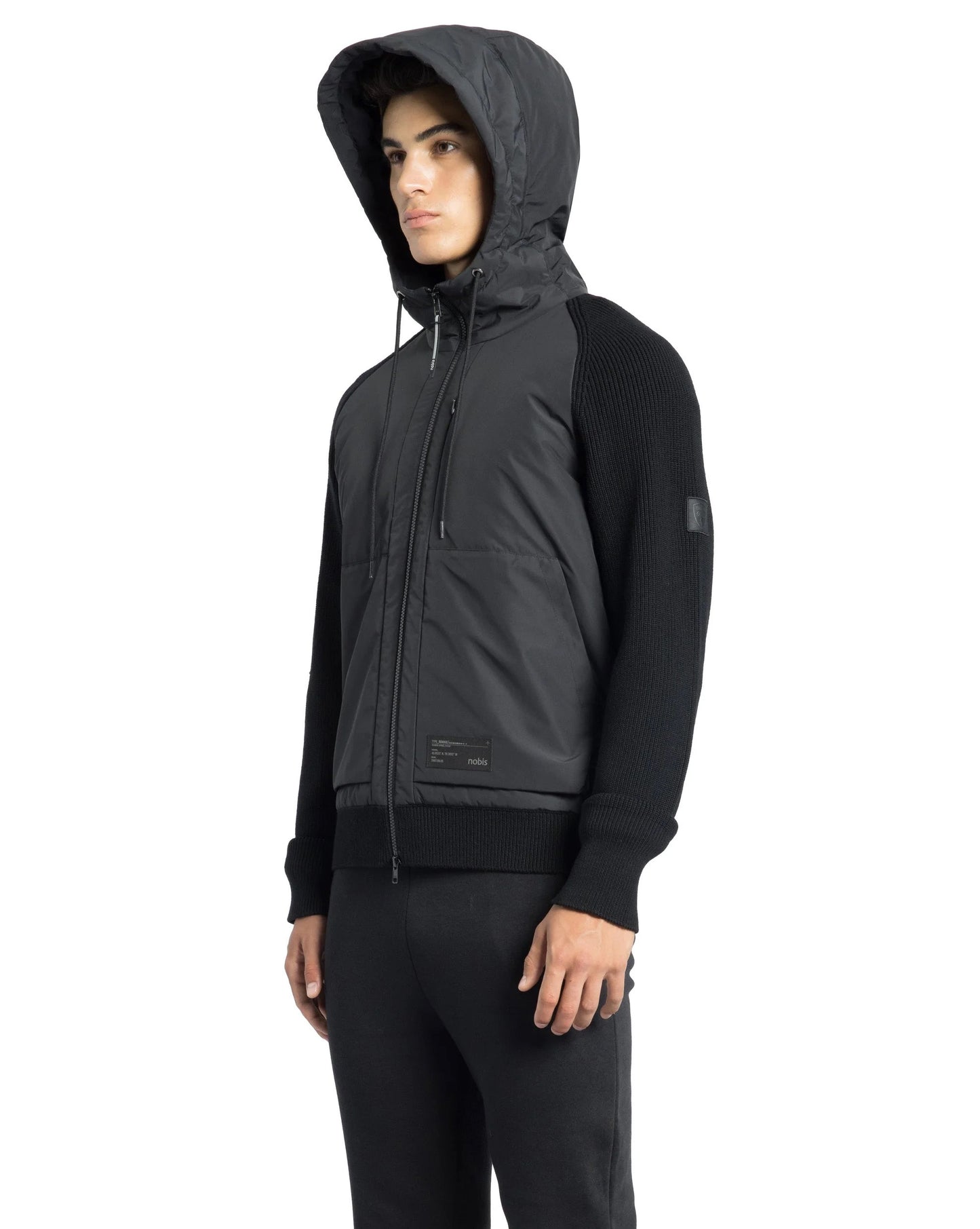 A person clad in the luxurious Hedge Men's Performance Hoodie by Nobis and black pants, standing sideways against a white background.