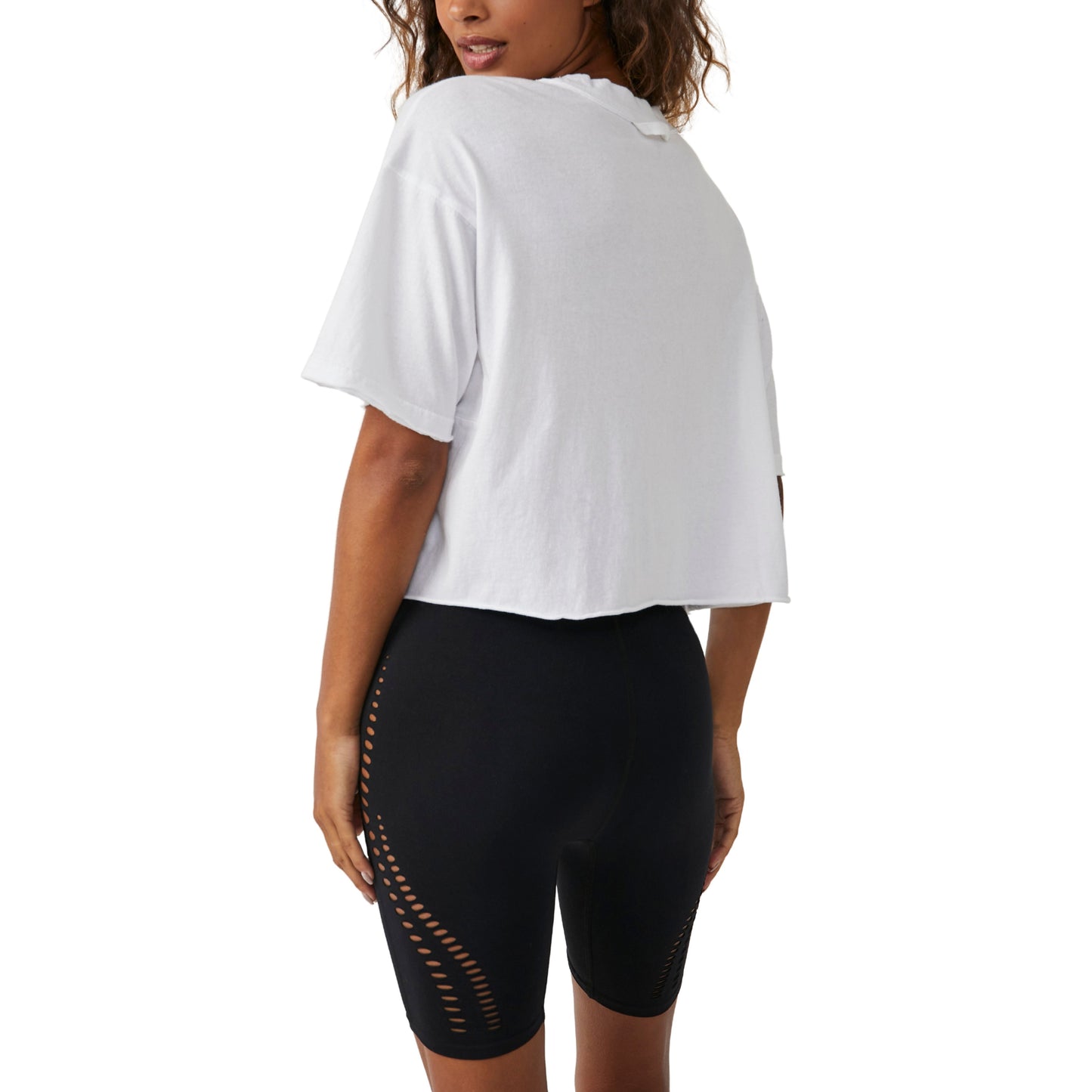 Woman from the back wearing a white Free People Movement "Inspire Tee" t-shirt and black cycling shorts with cut-out details along the legs.
