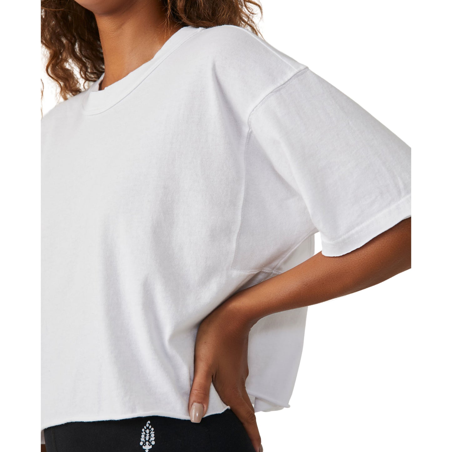 Close-up of a woman in a Free People Movement Inspire Tee in White, focusing on the sleeve and torso with her hand on her hip.