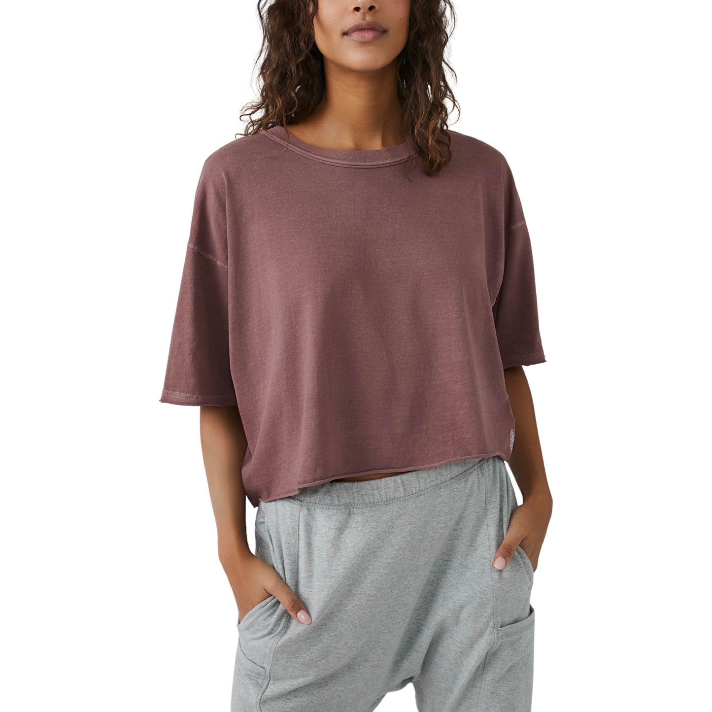 Woman wearing an oversized, maroon Free People Movement Inspire Tee and grey sweatpants, standing with one hand in her pocket.