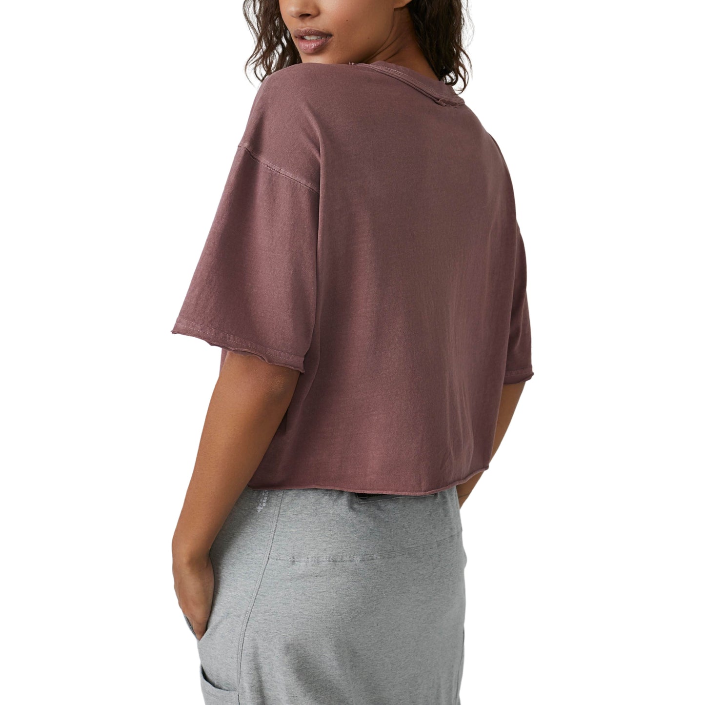 Back view of a woman wearing an oversized boxy fit Wild Mustang Inspire Tee in muted purple and light grey pants, focusing on the shirt's design and fit by Free People Movement.