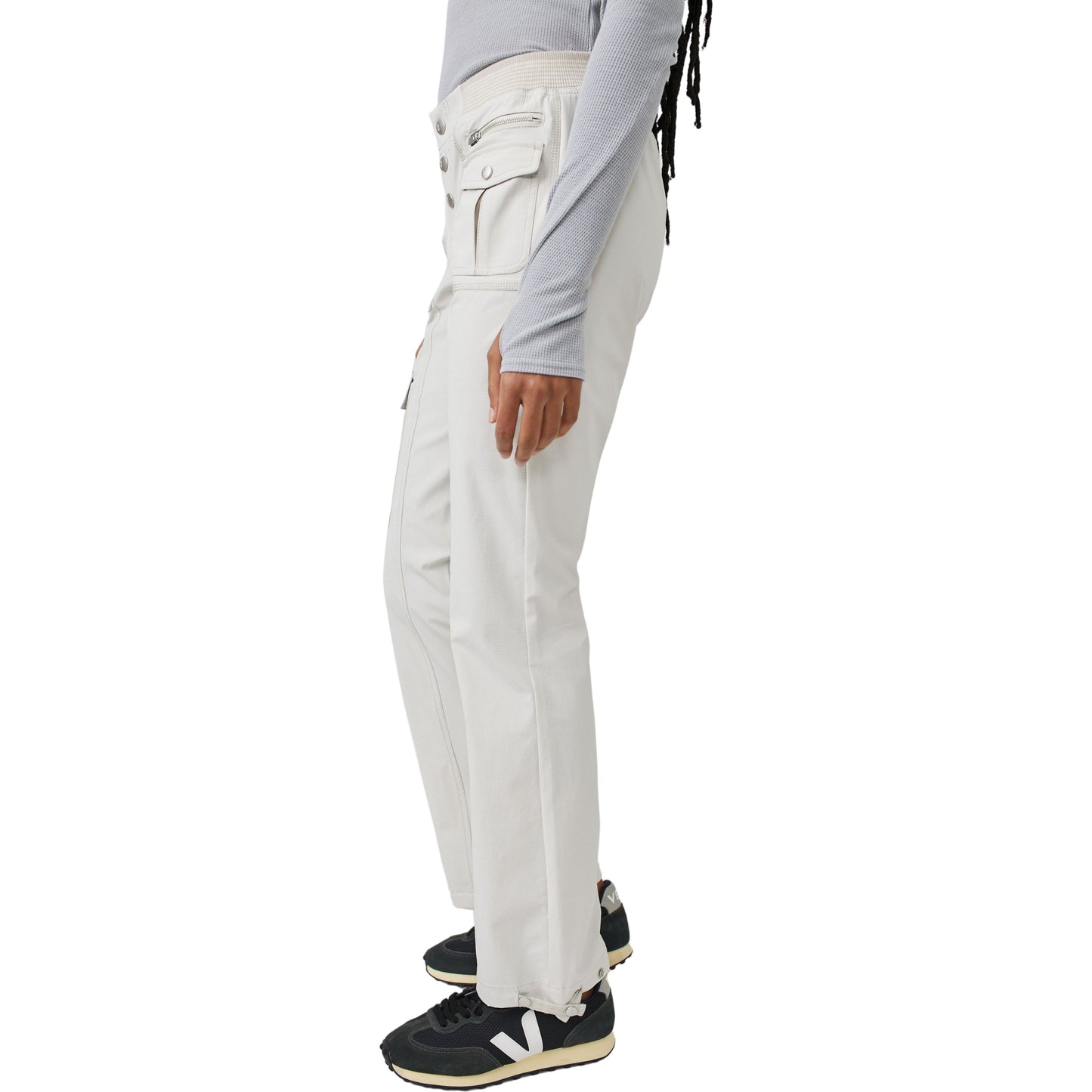 A person standing side-view wearing Cascade Flare pants in Muted Beige and Free People Movement black sneakers with white logos. Only the lower half of the body is visible.