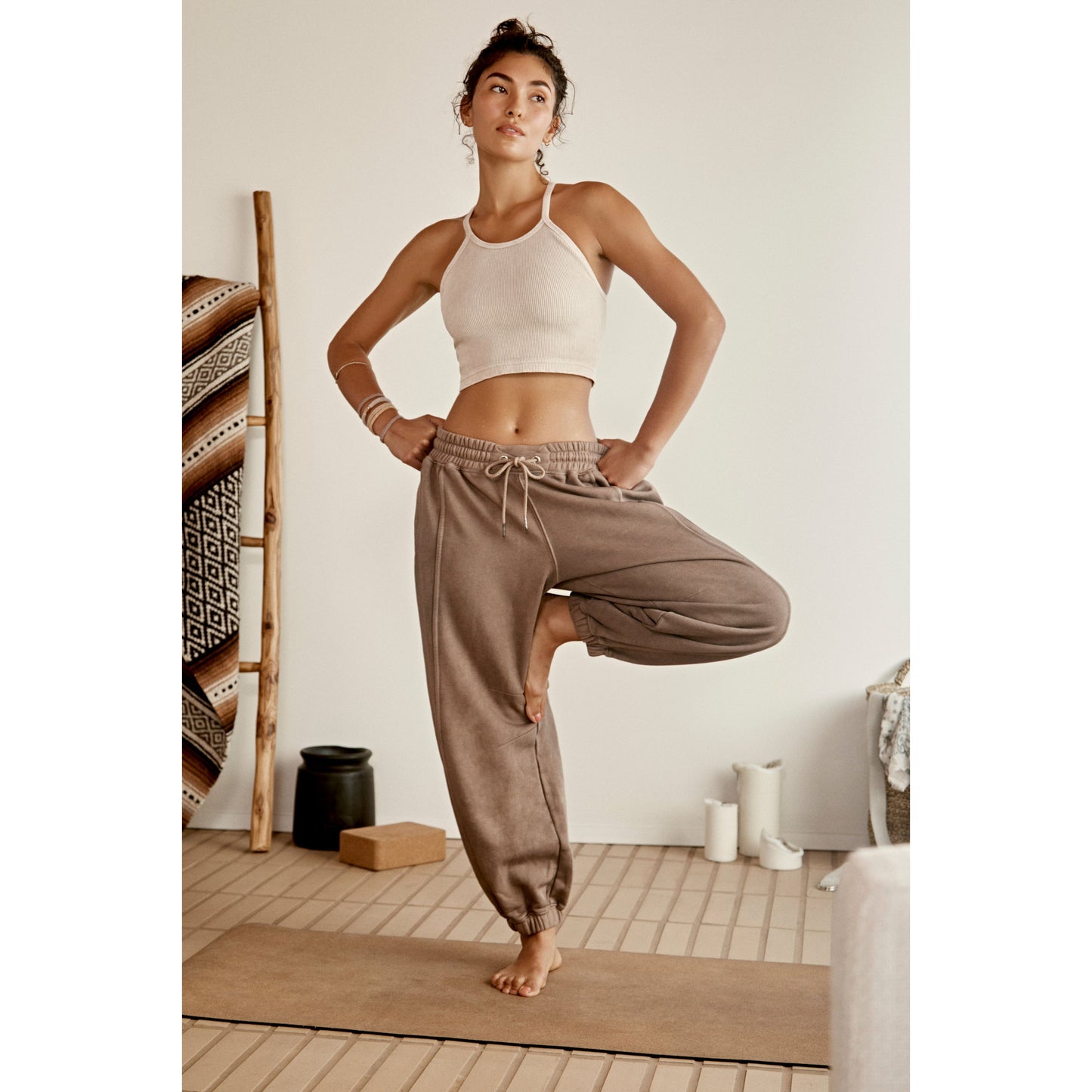 A woman in a white sports bra and Sprint To the Finish Pant, Hickory poses confidently with her hand on her hip in a well-lit room with neutral decor.