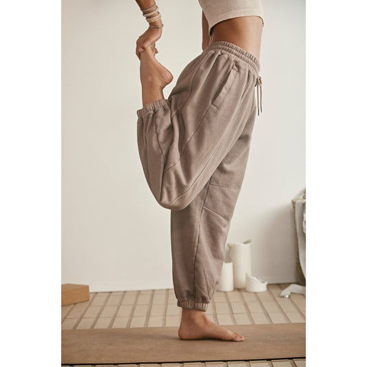 A person practices yoga in a beige room, standing on one foot while holding the other, dressed in Free People Movement's Sprint To the Finish Pant in Hickory.