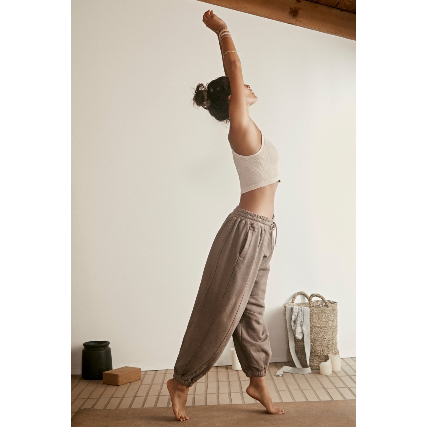 Woman in a white crop top and Sprint To the Finish Pant, Hickory by Free People Movement stretching in a sunlit yoga studio with wooden beams and minimalistic decor.