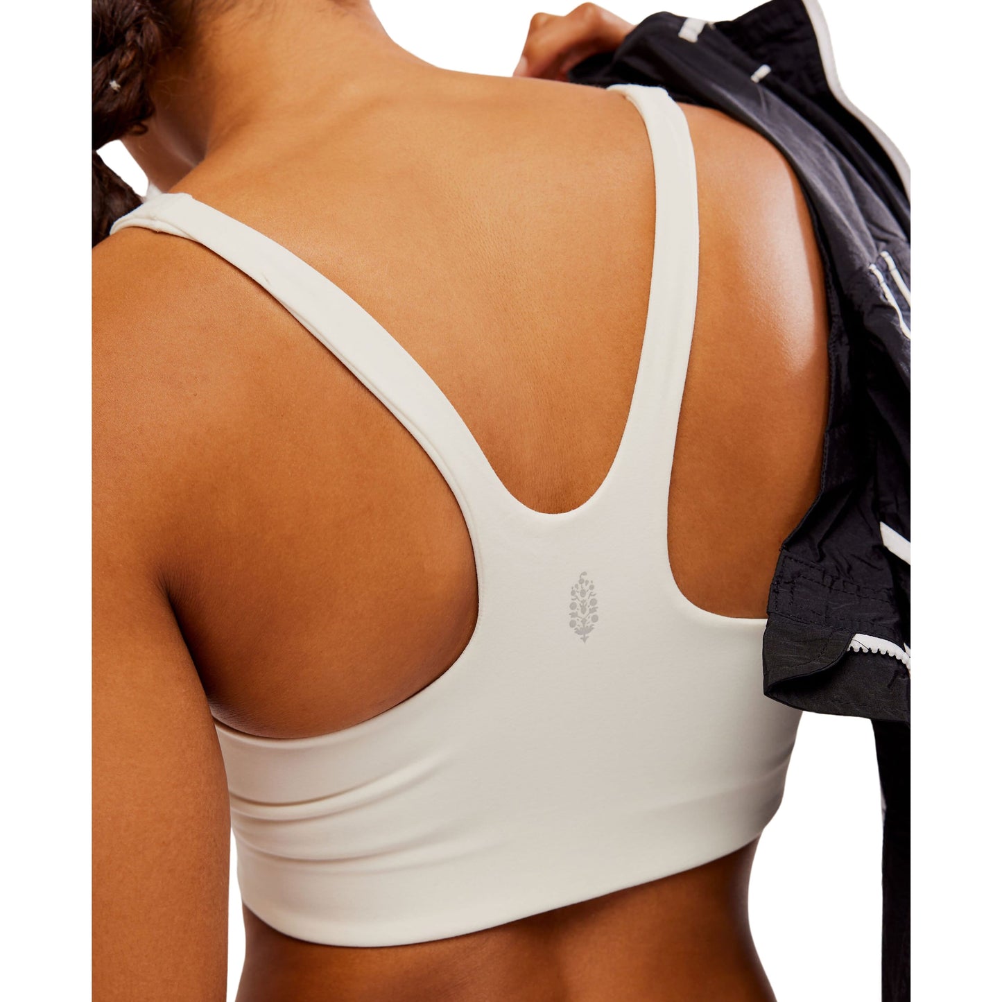 Close-up of a woman's back showing her wearing a white Free People Movement Never Better SQ Neck Bra with a racerback design and a small logo.