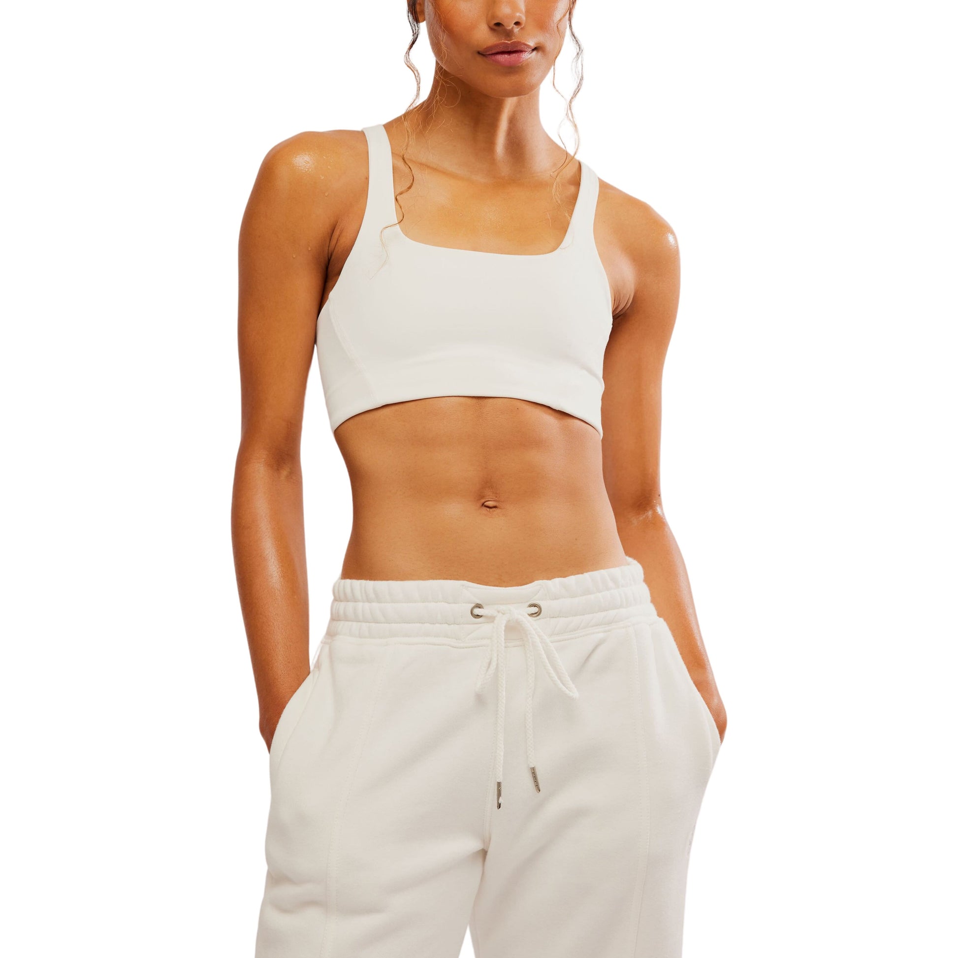 A woman wearing a Free People Movement Never Better SQ Neck Bra in White and cream drawstring joggers, standing with her hands on her hips.
