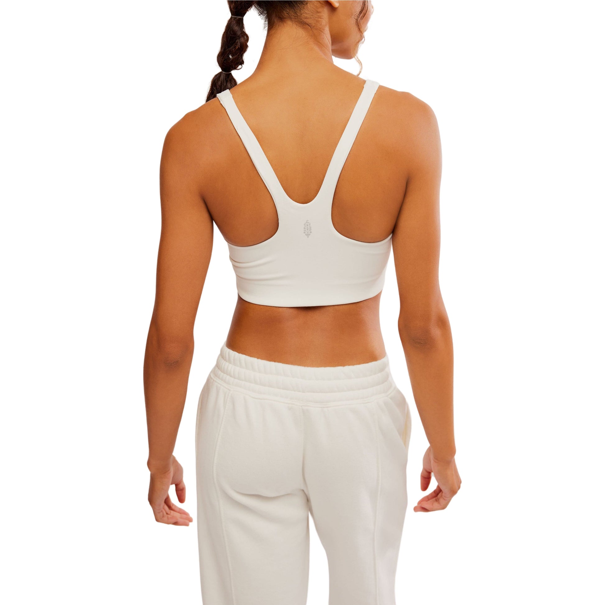 Rear view of a woman wearing a Free People Movement Never Better SQ Neck Bra in White and sweatpants, isolated on a white background.