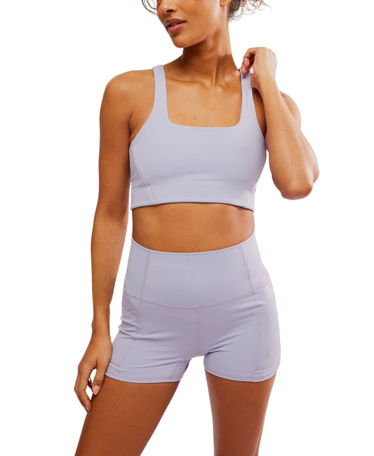 A woman wearing a Free People Movement Never Better SQ Neck Bra in Platinum and shorts set, standing with one hand adjusting her hair.
