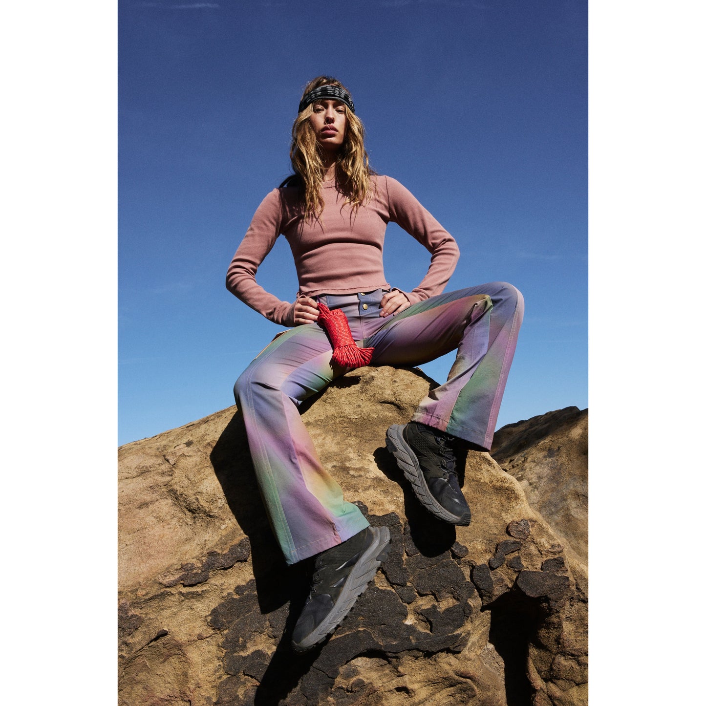 Woman in Free People Movement's Printed Cascade Flare pants, in the Galaxy Gradient print, posing on a rock under a clear blue sky.
