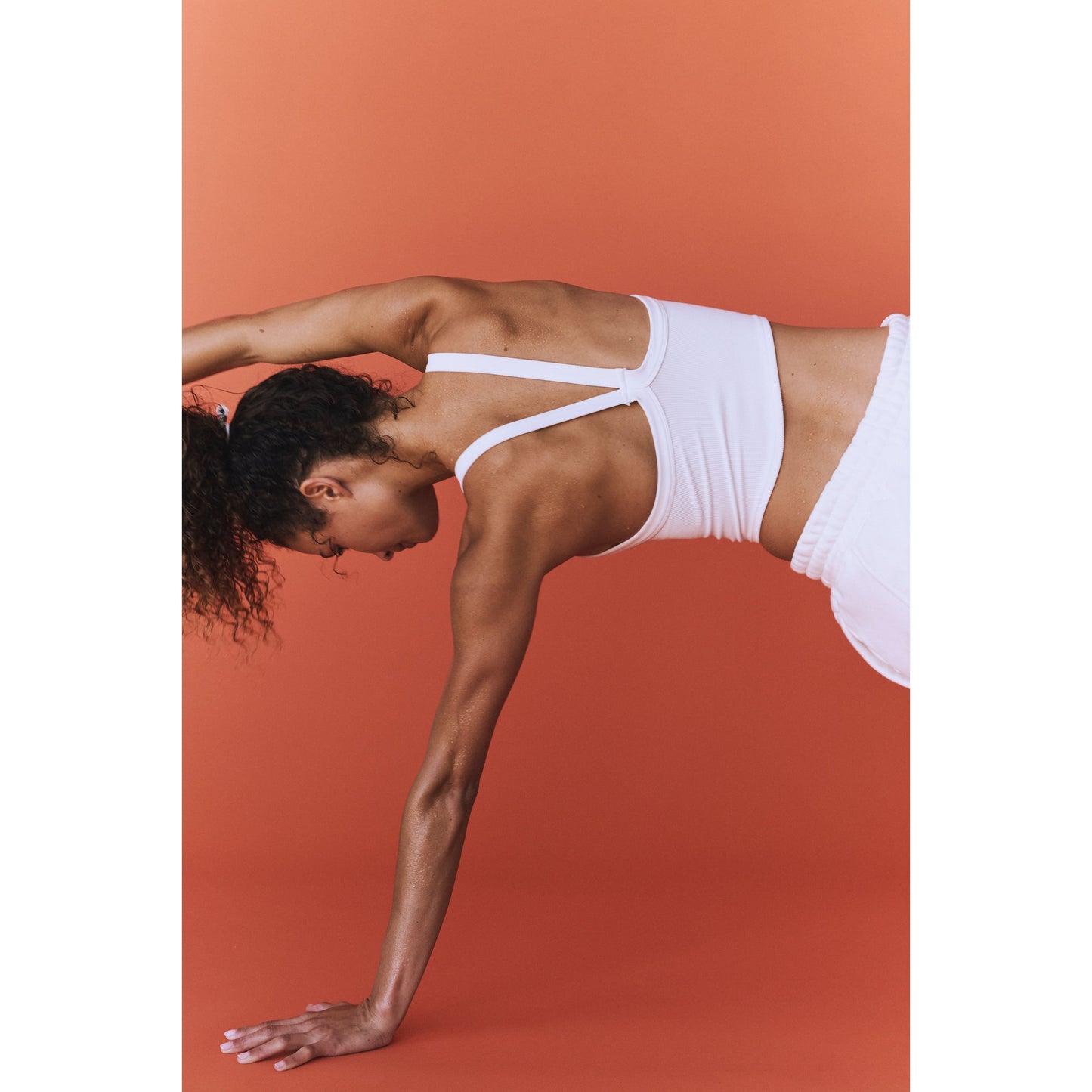A woman in an All Clear Cami Solid by Free People Movement performing a backbend against a red background.