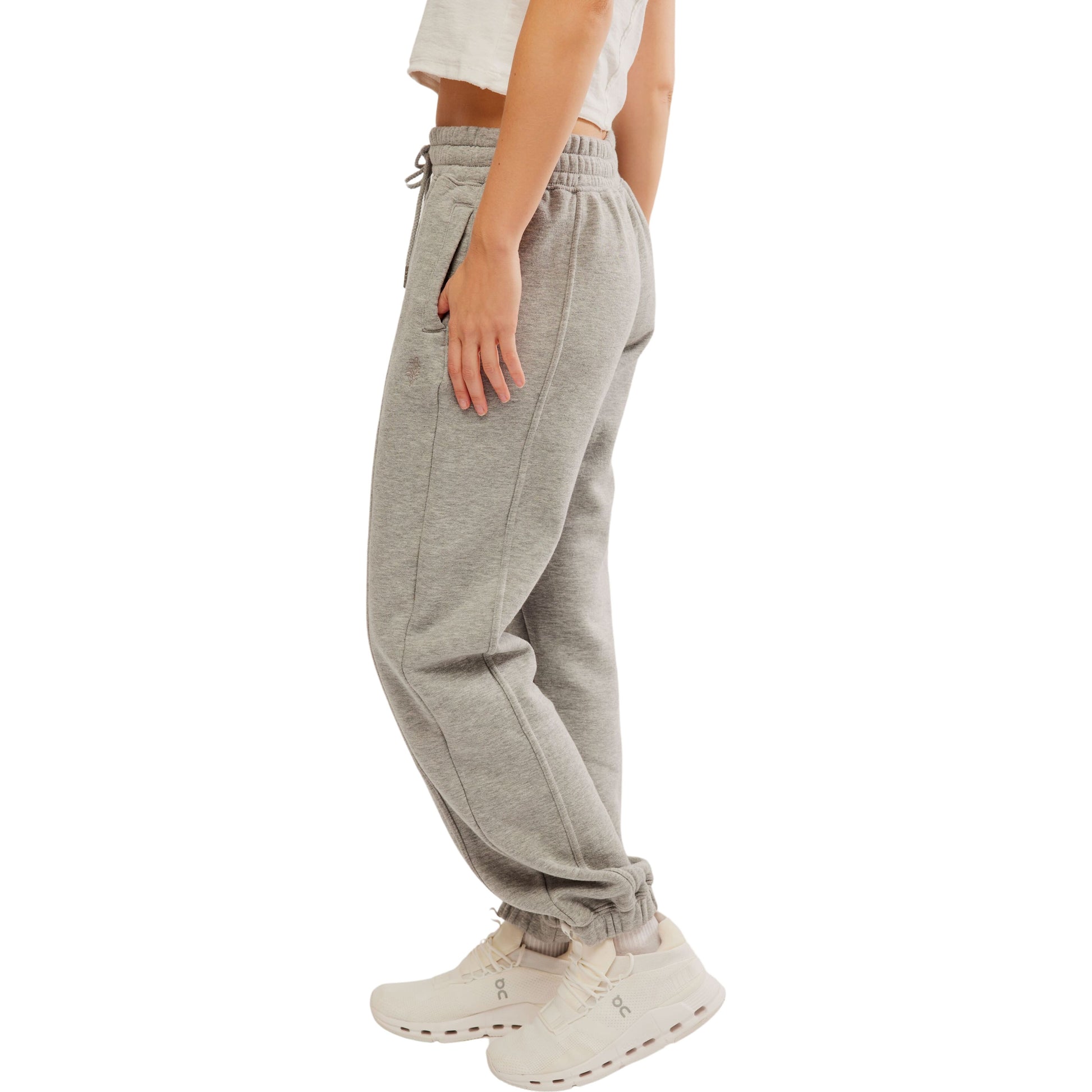 A side view of a person wearing Free People Movement's Sprint To the Finish Pant in Heather Grey and white sneakers, with their hand resting on their hip. White background.