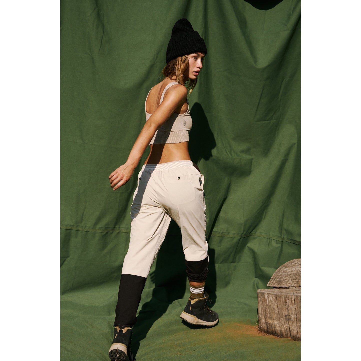 Young woman in Free People Movement's Cascade Jogger in Muted Beige and beanie hat posing against a green backdrop.