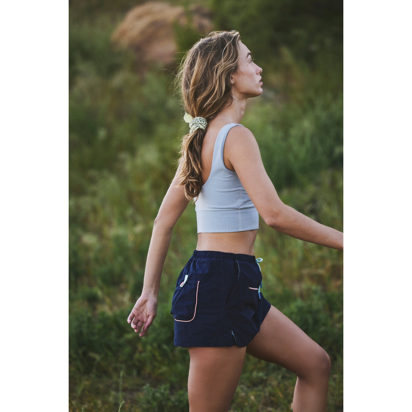 A young woman in Free People Movement athletic wear, including the Outskirts Skort in Midnight Navy Combo, walking outdoors, looking to the side with her hair in a ponytail.