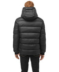 The figure, viewed from behind, wears the versatile Oliver Men's Reversible Puffer Jacket by Nobis. Its black hooded design effortlessly transitions from day to night, making it a two-in-one essential that Oliver would find perfect for any occasion.