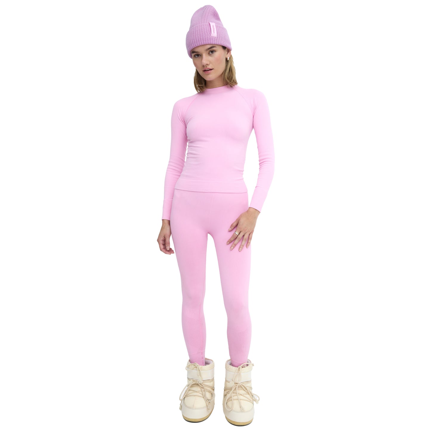 A person wearing Halfdays' Sophia Legging paired with a pink long-sleeve top, purple beanie, and white boots, standing against a white background.
