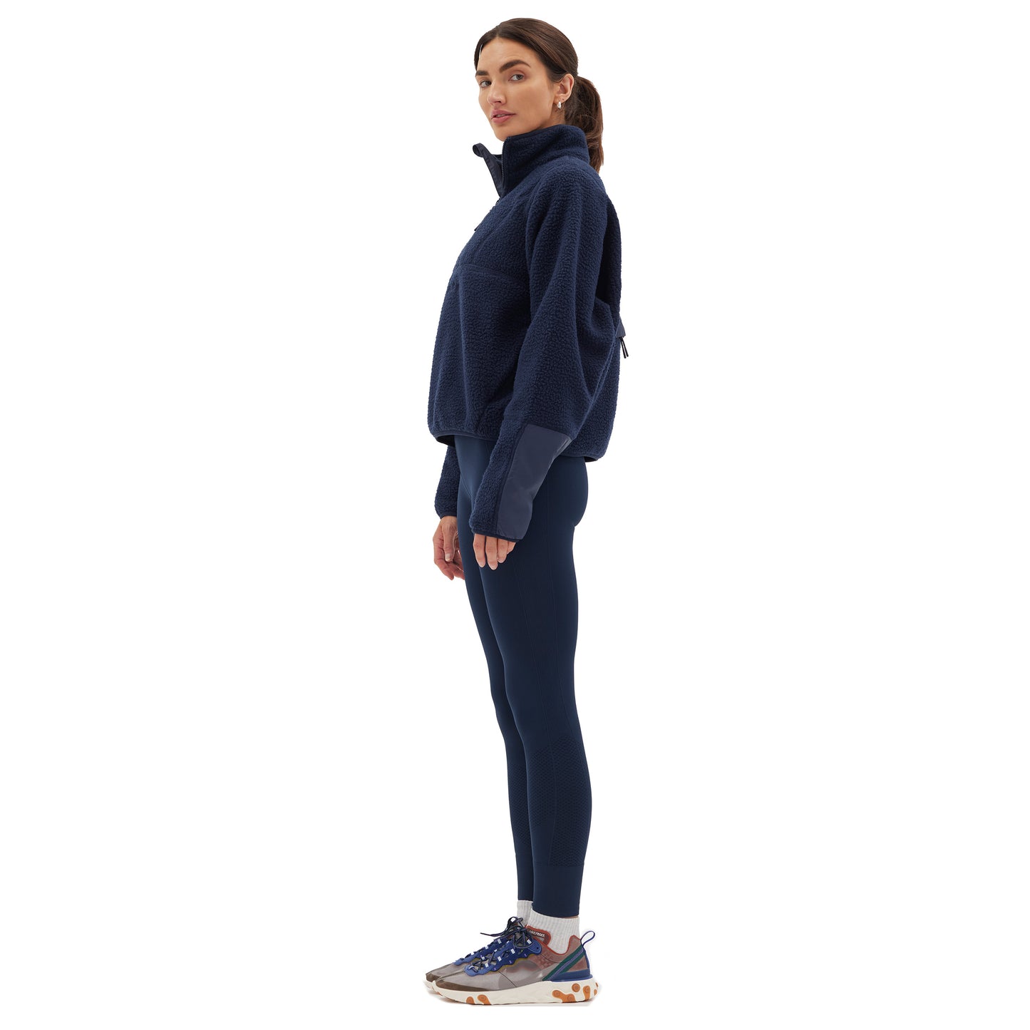 A person in a navy Pieper Fleece by Halfdays, leggings, and sneakers stands sideways against a white background.