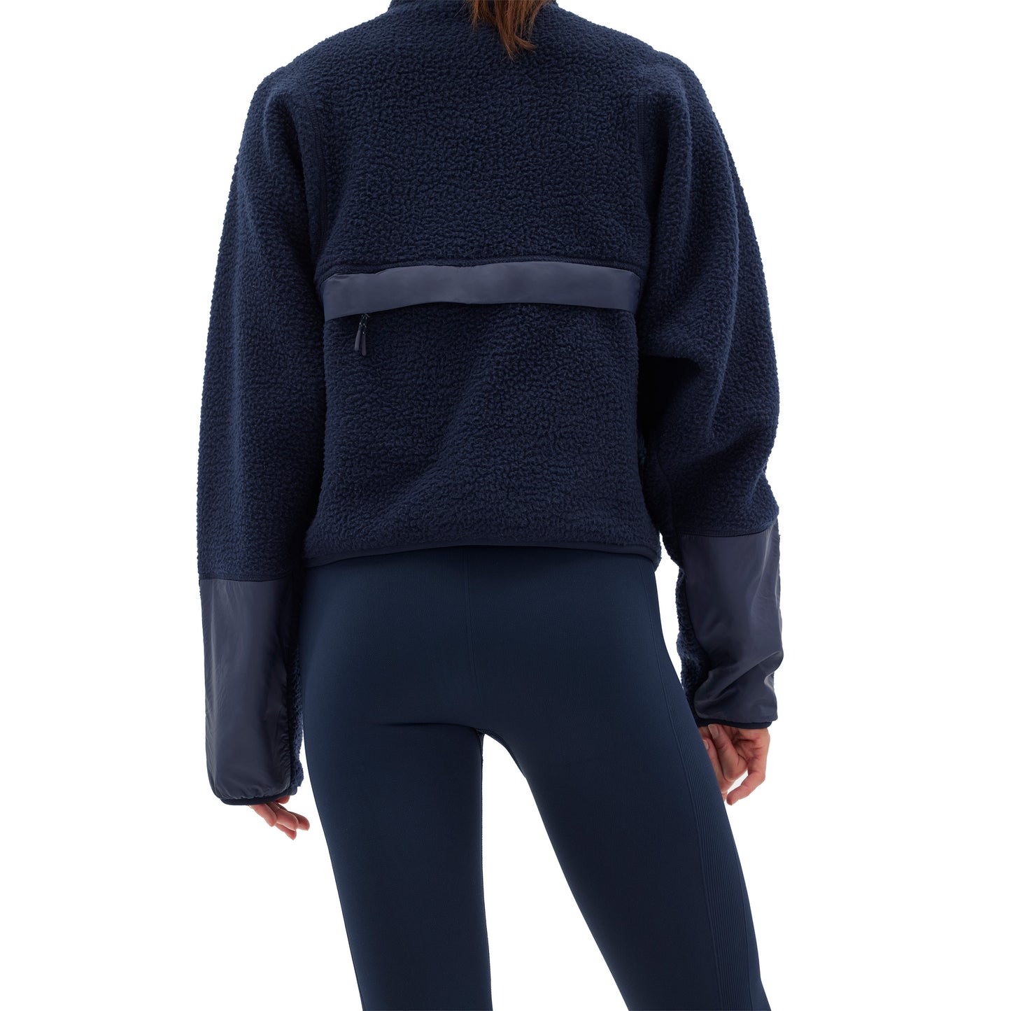 A person wearing the Pieper Fleece by Halfdays, featuring a navy blue quarter-zip design with contrasting cuffs and a horizontal back band, is shown from the back while paired with dark leggings.