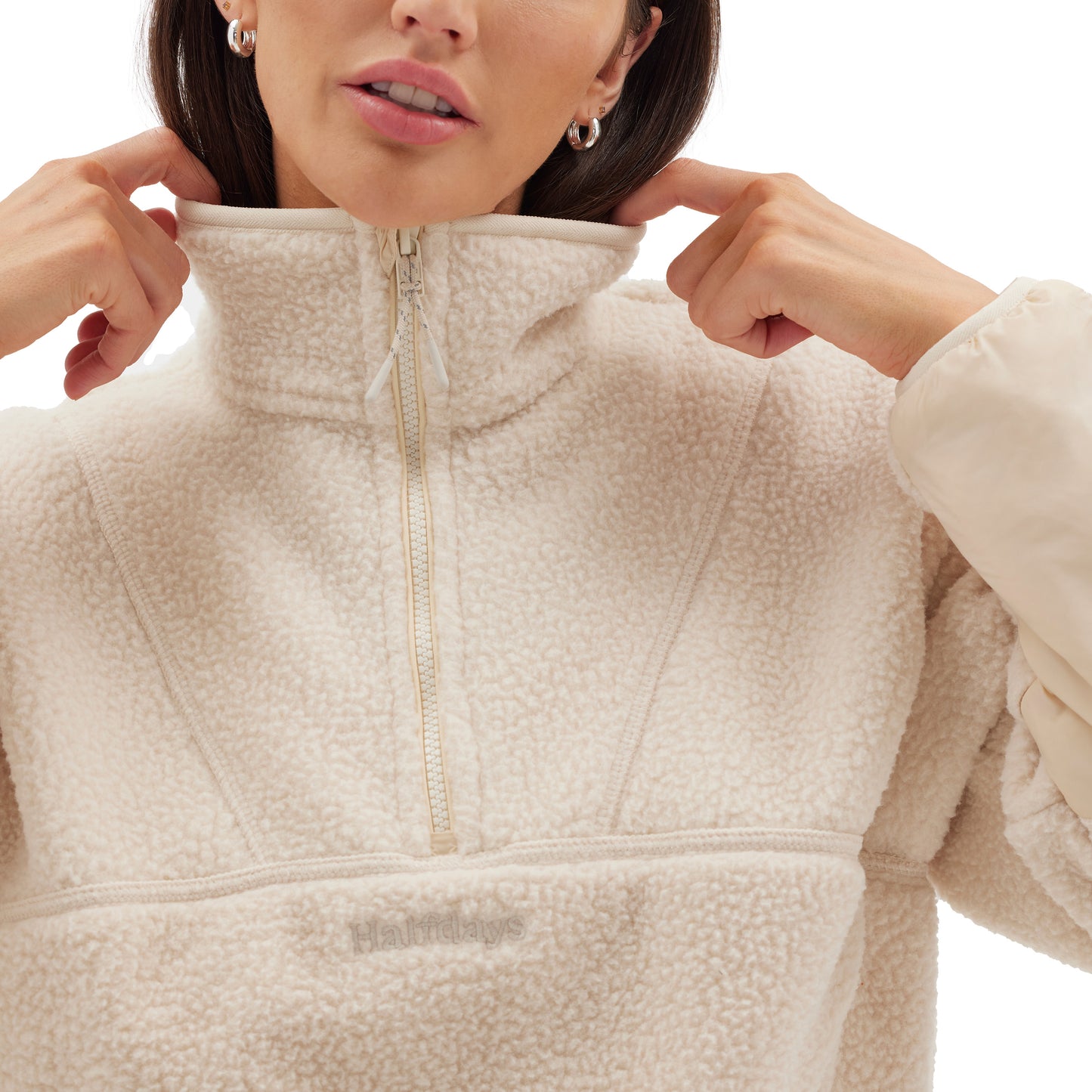 A person wearing the Pieper Fleece from Halfdays, a light-colored Sherpa pullover with a quarter-zip, adjusts the collar with both hands.