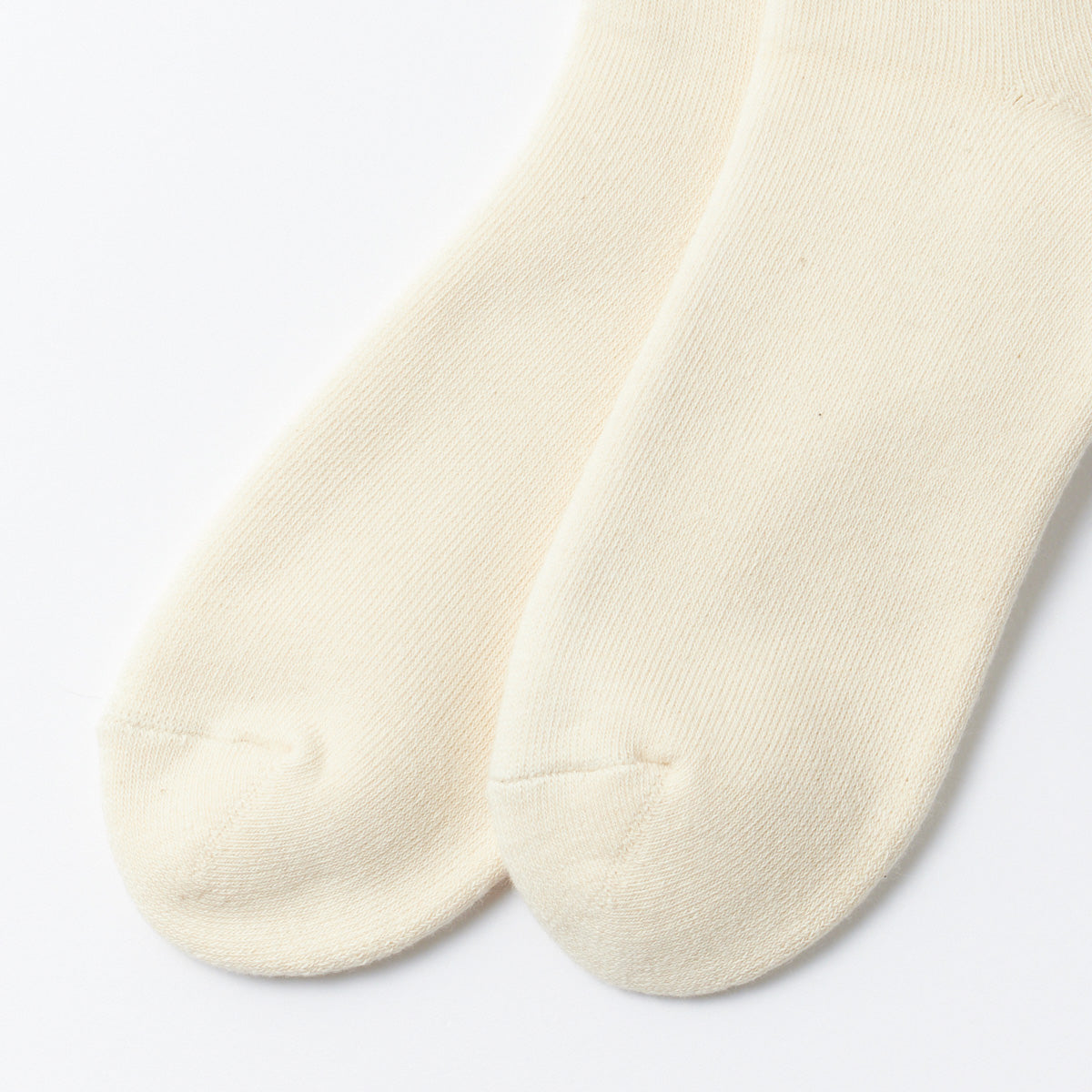 A pair of RoToTo Organic Daily Ribbed Crew Socks in Ecru lies on a white surface.