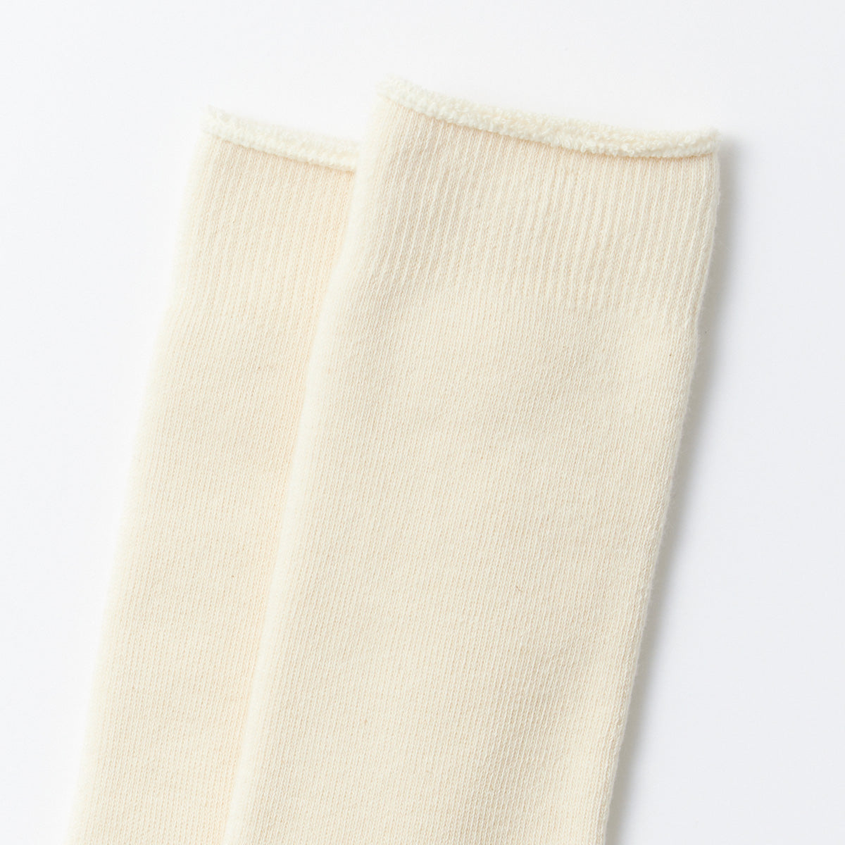 Close-up of two ecru socks from the Organic Daily 3 Pack Ribbed Crew by RoToTo, showcased on a white background.