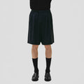 A person stands against a plain background wearing Seven Gauge's Tropical Wool Basket Short with an adjustable waist strap, along with black socks and shoes. Their upper body remains out of view.