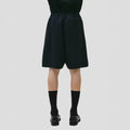A person in Seven Gauge's Tropical Wool Basket Short with adjustable waist, black socks, and comfy fit black shoes stands against a white background.