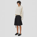 The person wears a beige hoodie, a Tropical Wool Basket Short by Seven Gauge, and black loafers while standing against a plain white background, exuding a comfort fit.