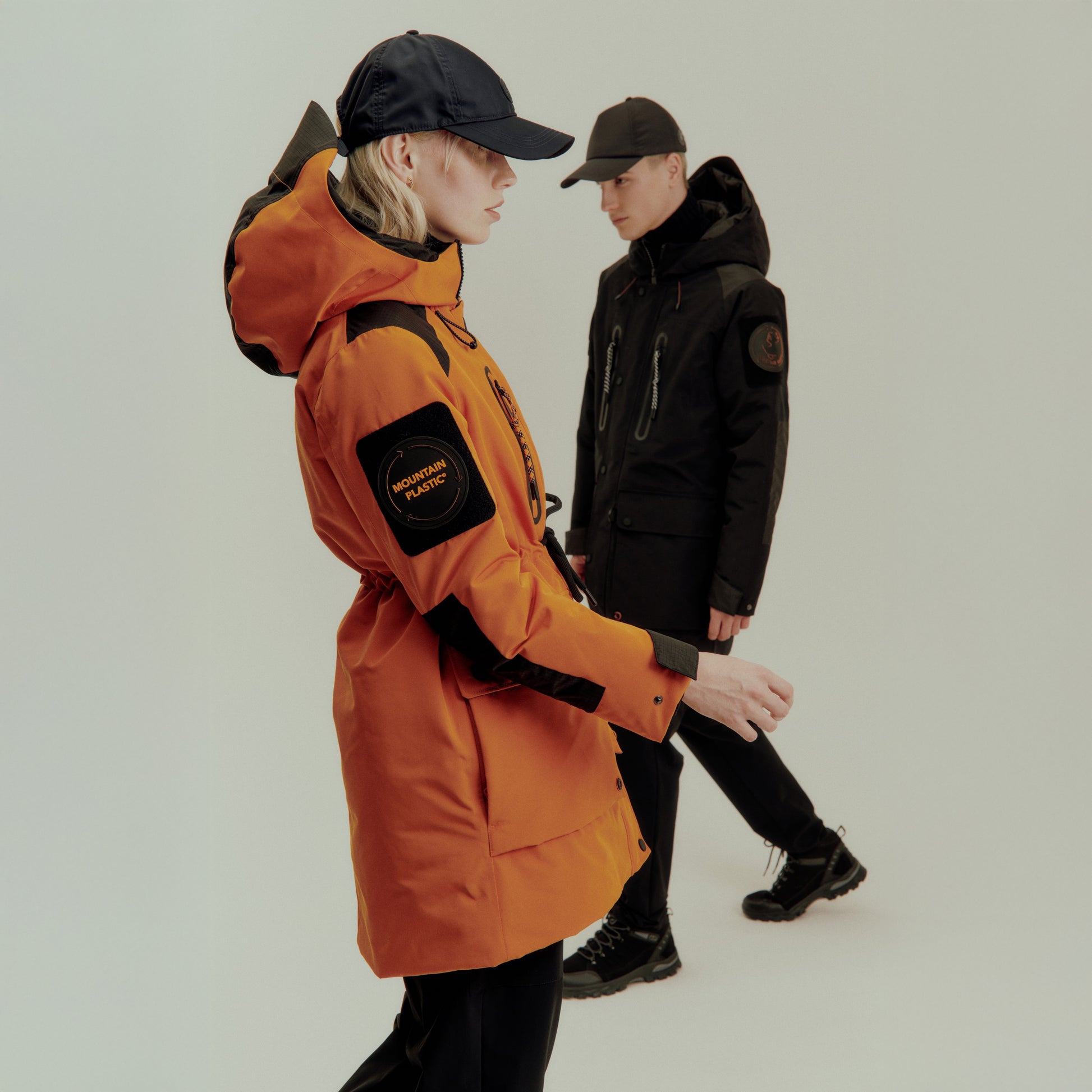 Two people wearing orange and black jackets with visible branding on a light gray background