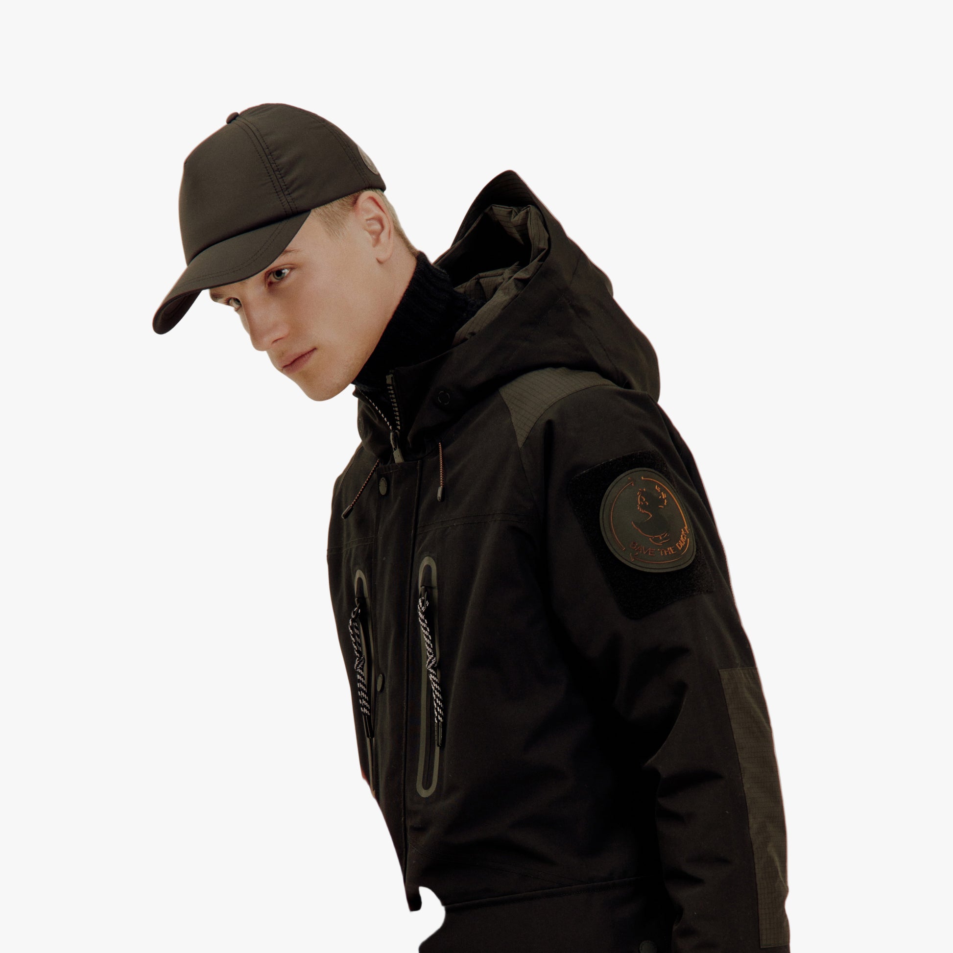 Person wearing a black jacket and cap with a blurred orange garment in the foreground.