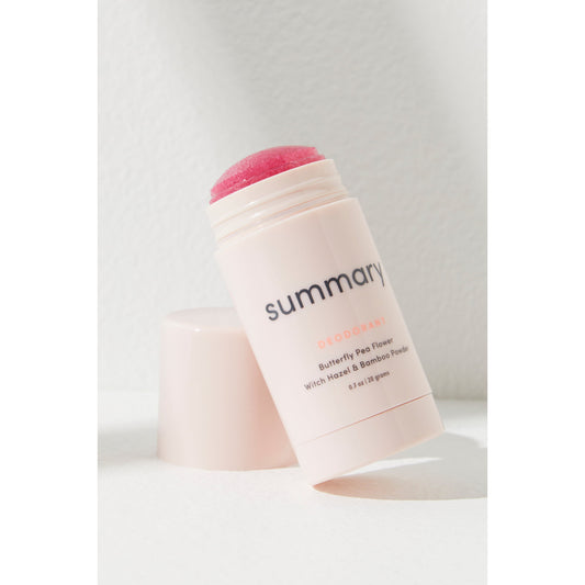 Pink Summary Deodorant stick labeled "Free People Movement" with cap off, leaning against a white wall in bright sunlight.