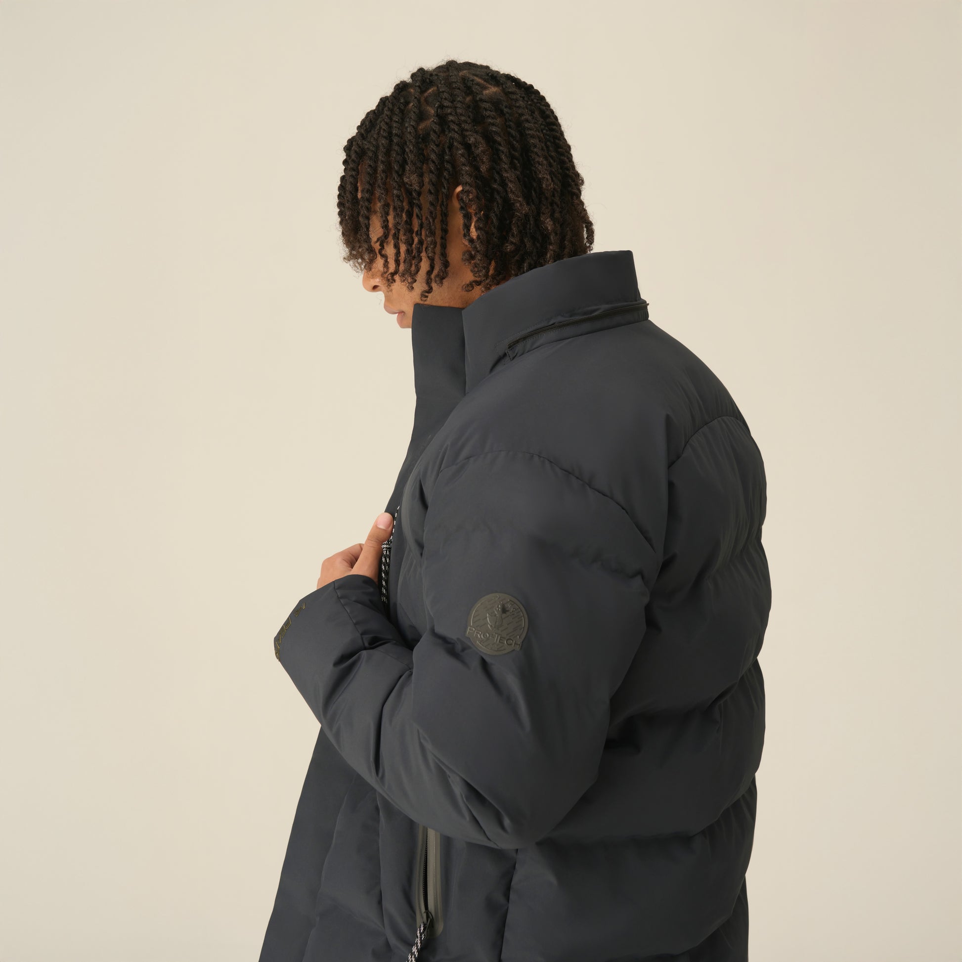 Person wearing a dark puffer jacket on a beige background