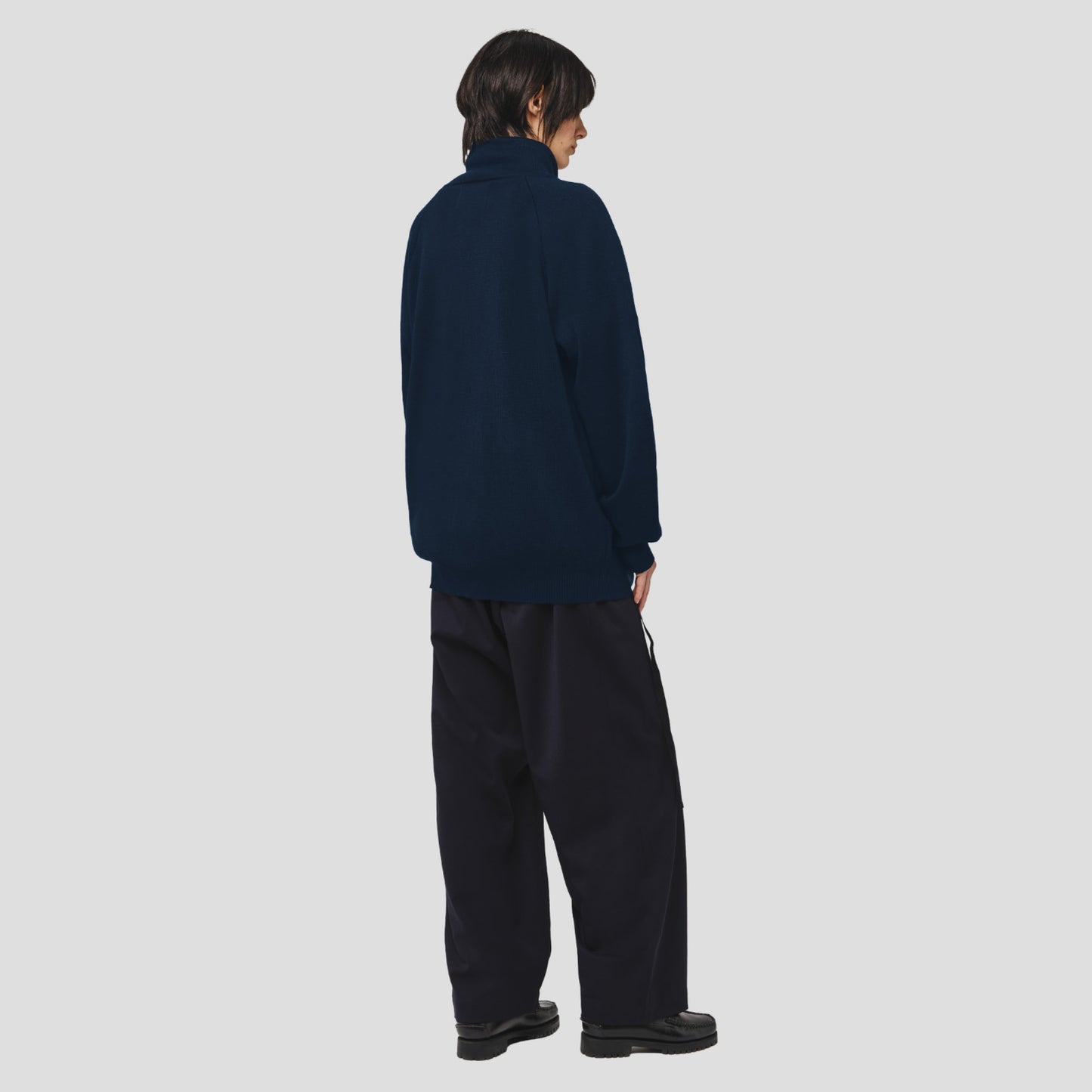 A person stands with their back to the camera, wearing the Seven Gauge Wool Cotton Full Zip Sweater in Blu against a plain light gray background.