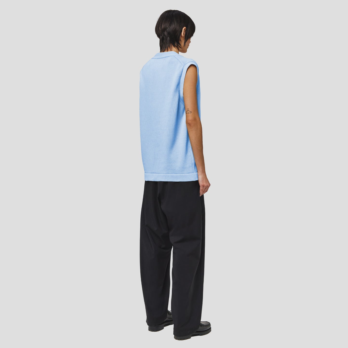 A person wearing a Seven Gauge Cotton Vest Sweater in blue and black wide-leg pants faces away against a white background.