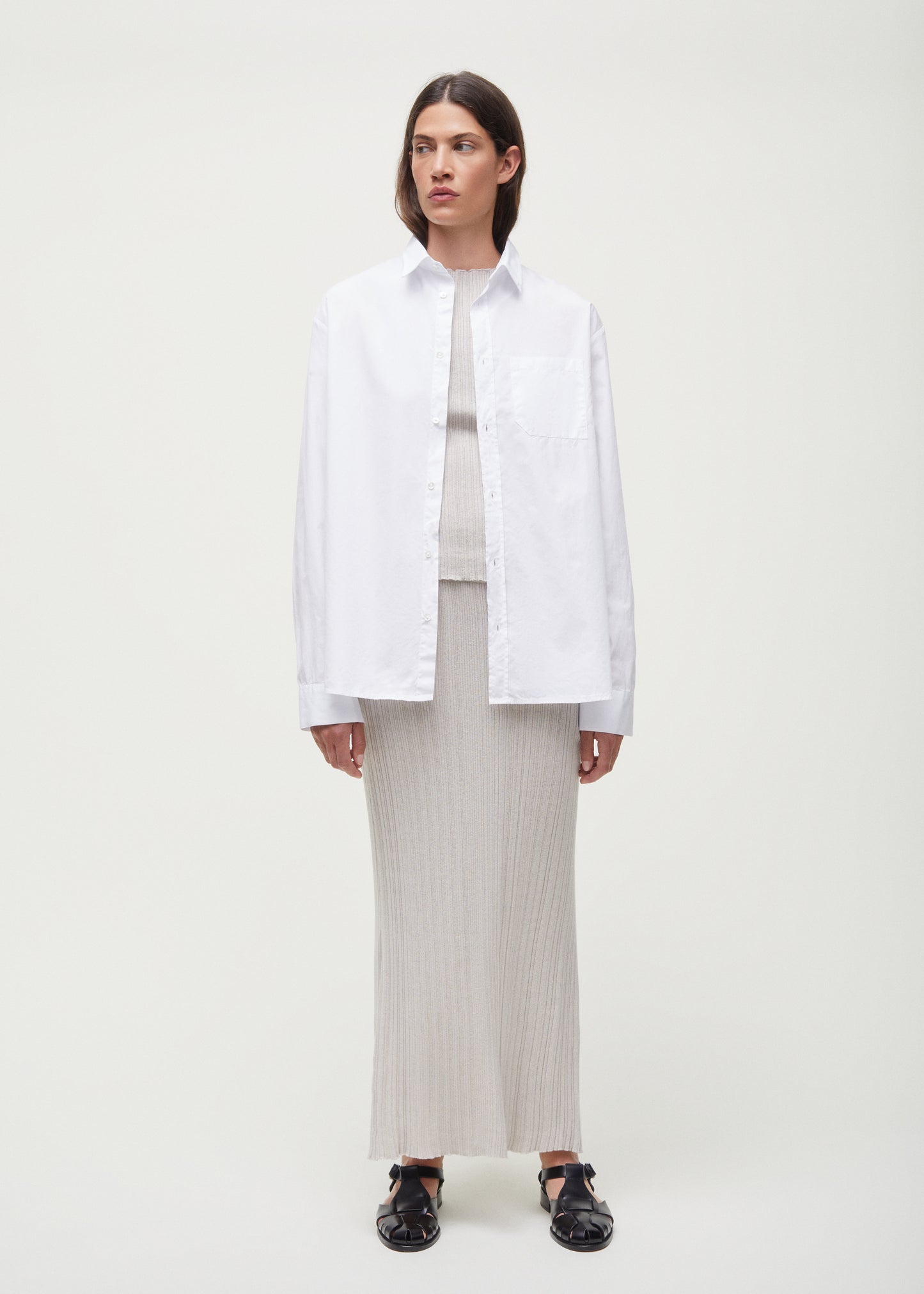 A person stands against a plain background wearing a white button-up shirt over the Seinne Linen Skirt by Aiayu, made from European organic cotton, paired with black shoes. Their hands rest at their sides.