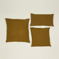 Three cushions on a light surface; two square "Simple Linen Pillows - 18x18, Bronze" by Hawkins New York and one rectangular, made from soft European linen.