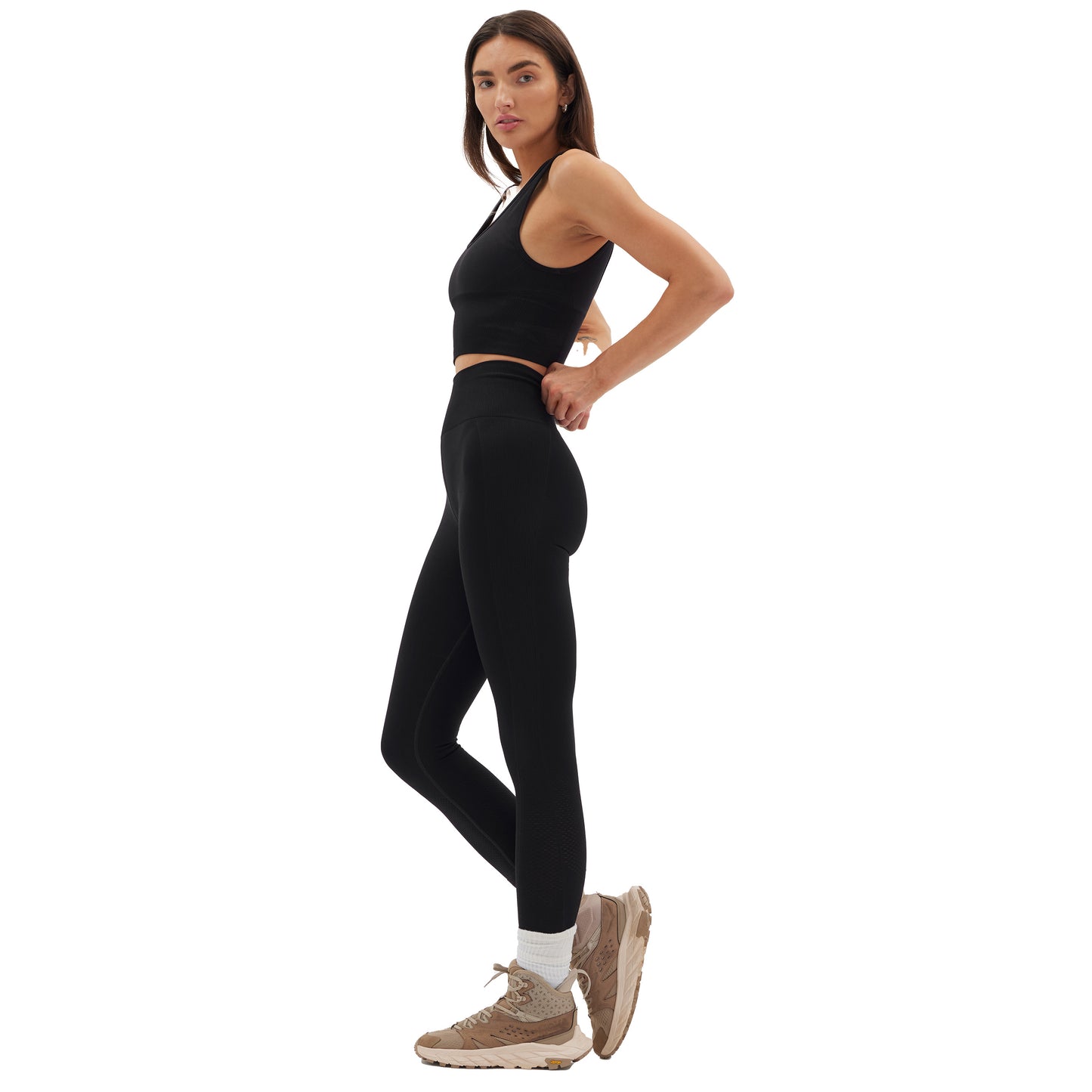 A person wearing the Halfdays Sophia Legging in a sleek black sports outfit paired with beige sneakers stands on one foot against a plain white background.