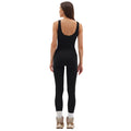 Wearing sleek black Sophia Leggings by Halfdays, the woman stands with her back to the camera against a white background. Complemented by seamless nylon sneakers, she's set for any outdoor adventure that awaits her.