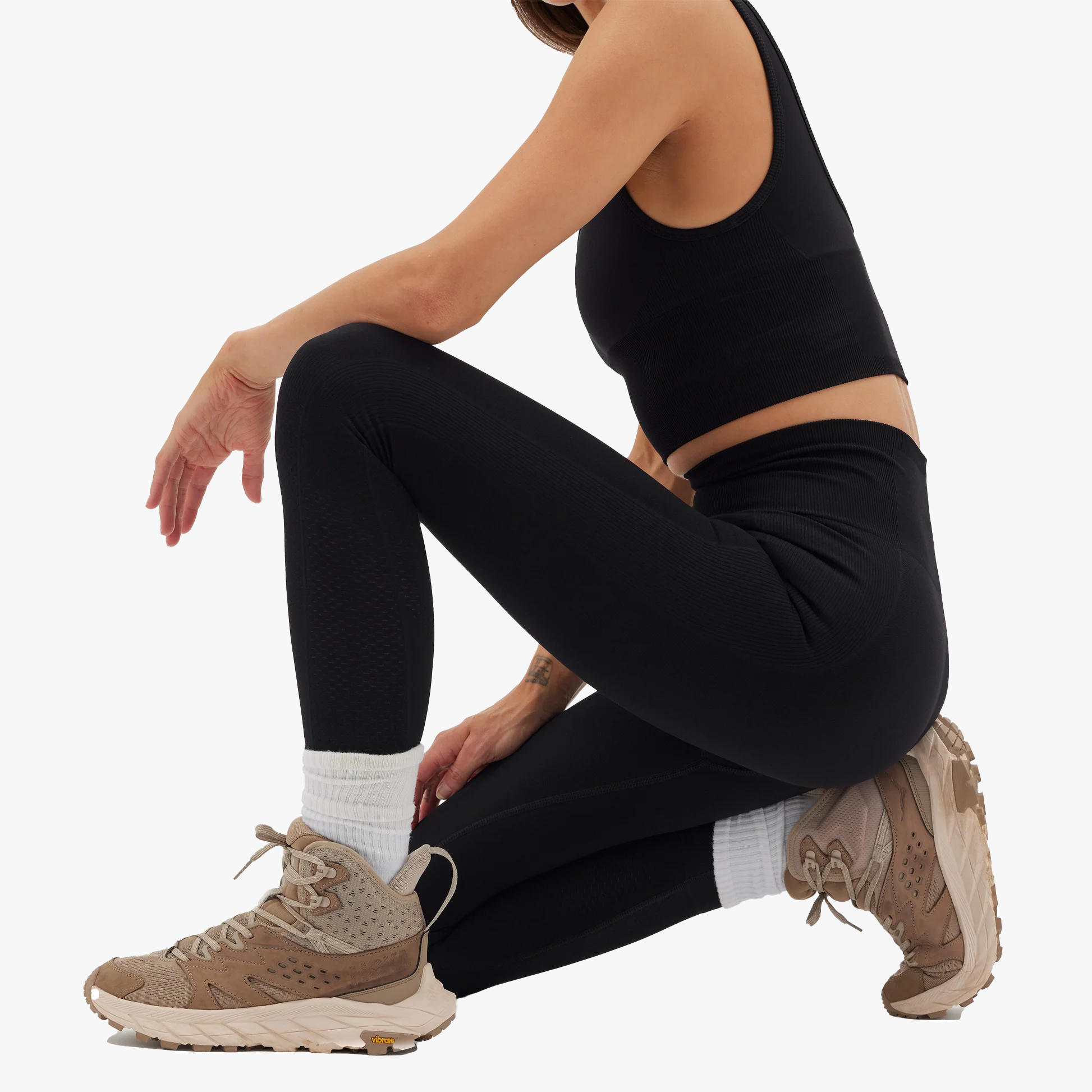 Person wearing black athletic leggings and brown sneakers on a white background
