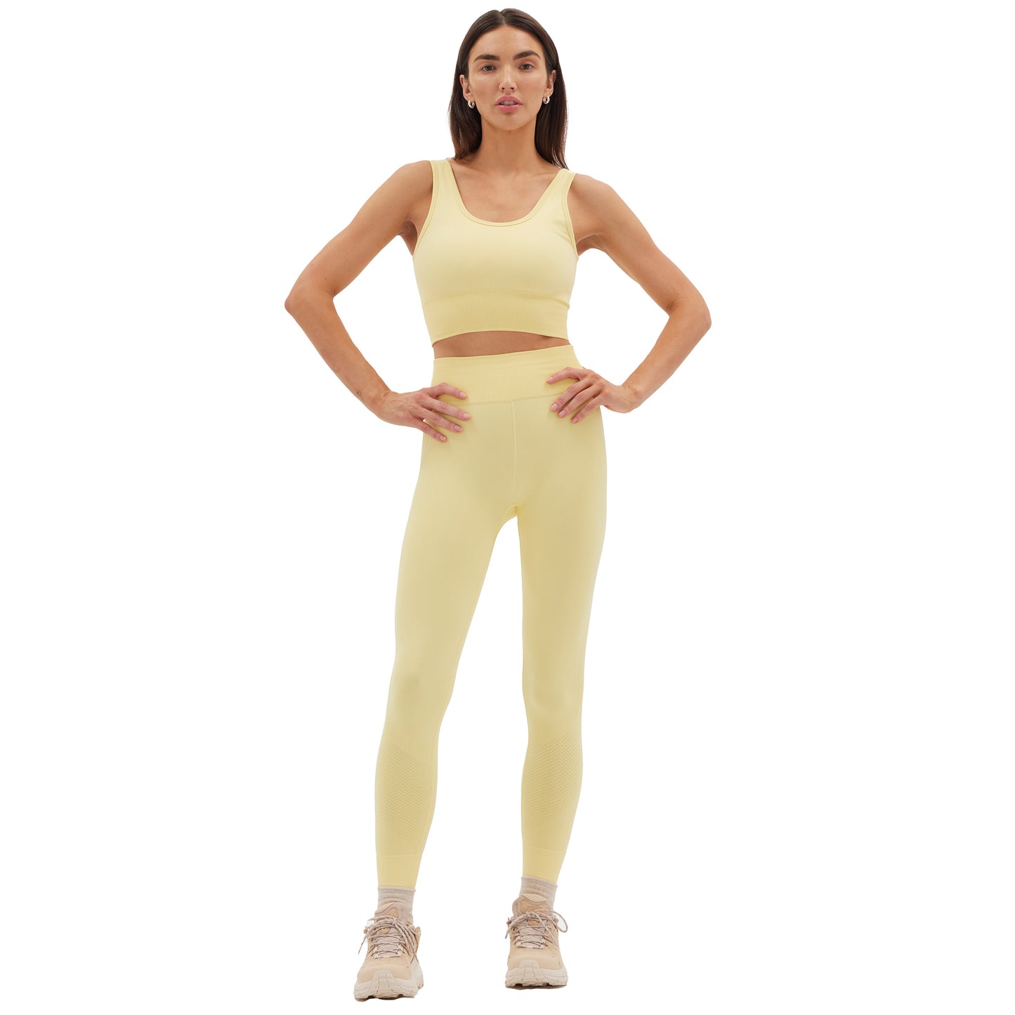 A person in pale yellow athletic wear, featuring the Sophia Legging by Halfdays, stands confidently with hands on hips against a white background.