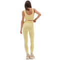 A woman in a yellow athletic outfit stands confidently with her back turned, hand on hip, wearing sneakers. Her Sophia Legging from Halfdays, crafted from seamless nylon, is ideal for any outdoor adventure.