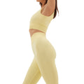 A person in a yellow athletic outfit and the compressive Sophia Legging by Halfdays stretches gracefully, arms raised and head tilted back, ready for an invigorating outdoor adventure.