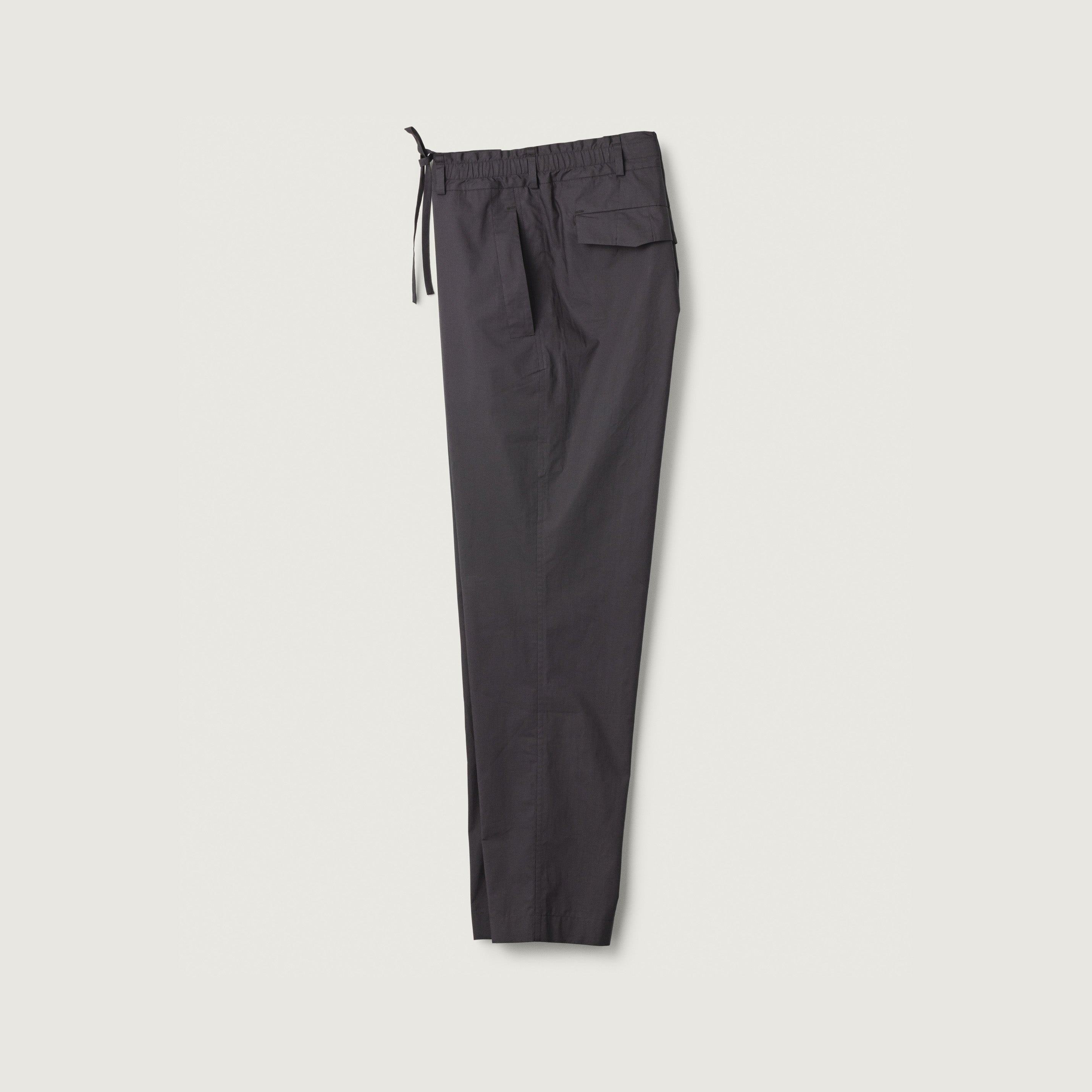 The Tom Trouser in Ink Poplin by Jan Machenhauer features black drawstring pants with an elastic waistband and a side flap pocket, shown laid flat on a white background.