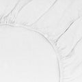 Close-up of the Simple Linen Fitted Sheet - Queen by Hawkins New York in stonewashed white, featuring gathered elastic edges and soft creases.