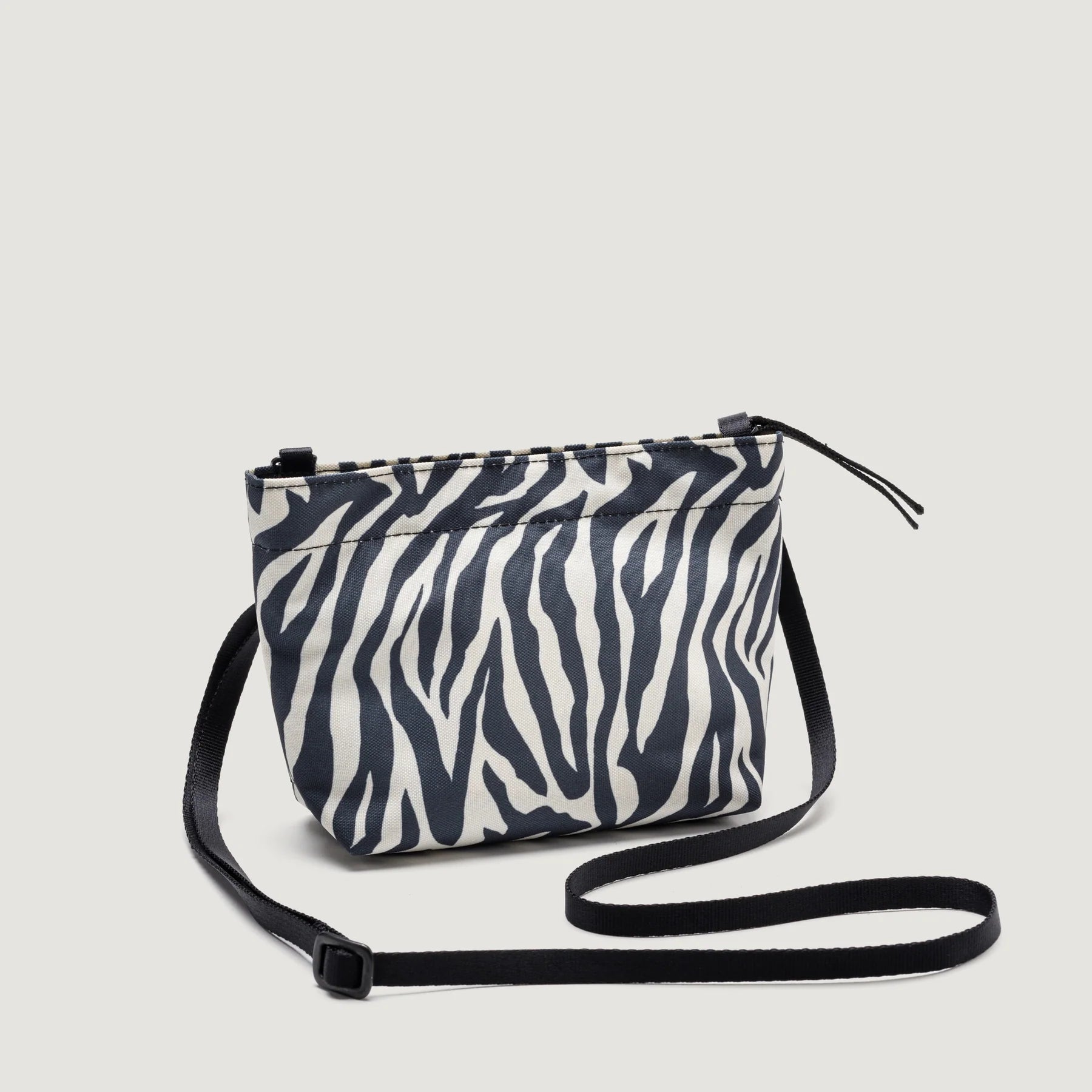A small Zipper Pouch Mini in Zebra print with a black adjustable strap, displayed against a white background by Bags in Progress.