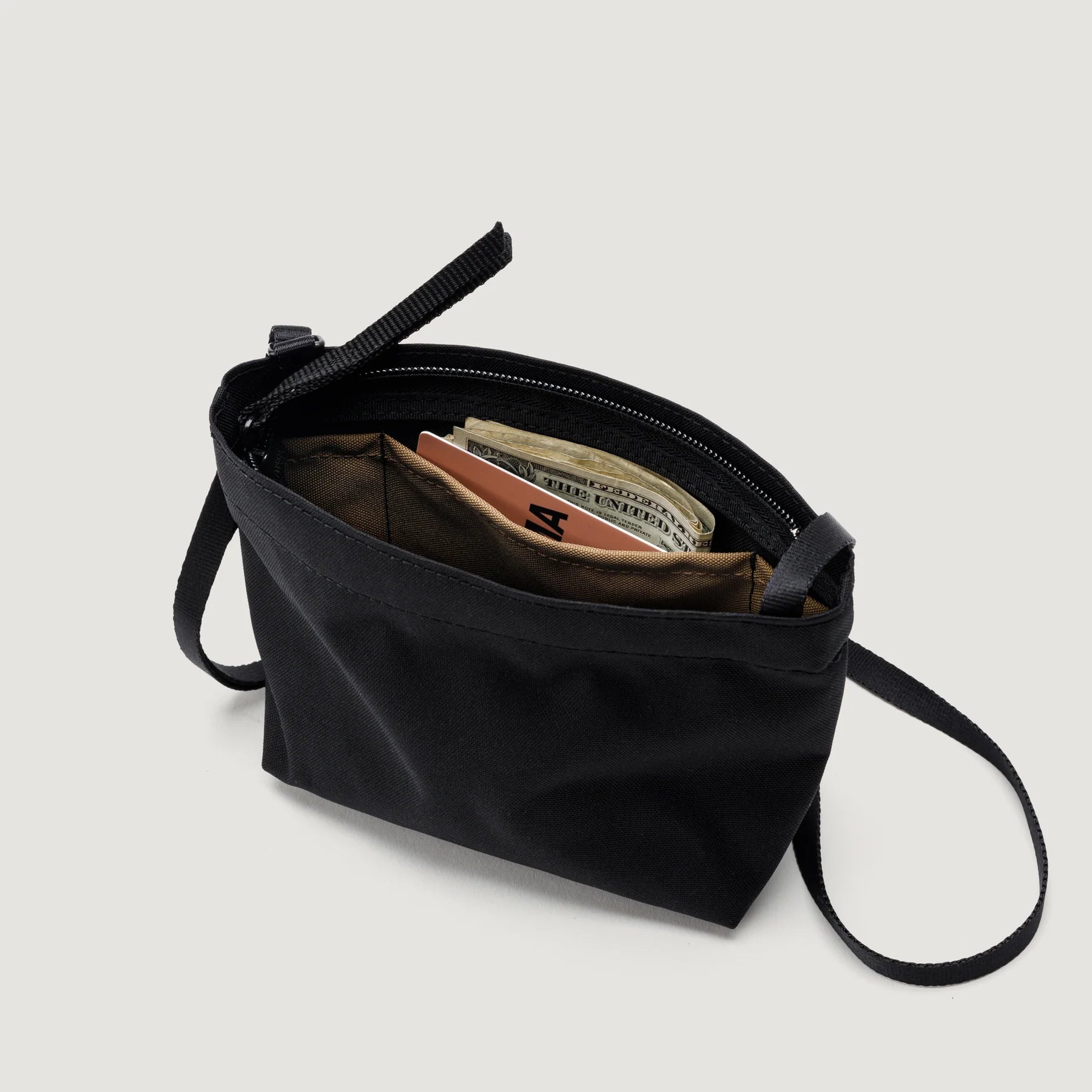 A small black Bags in Progress Zipper Pouch Mini partially open, revealing money and cards inside, against a plain white background.