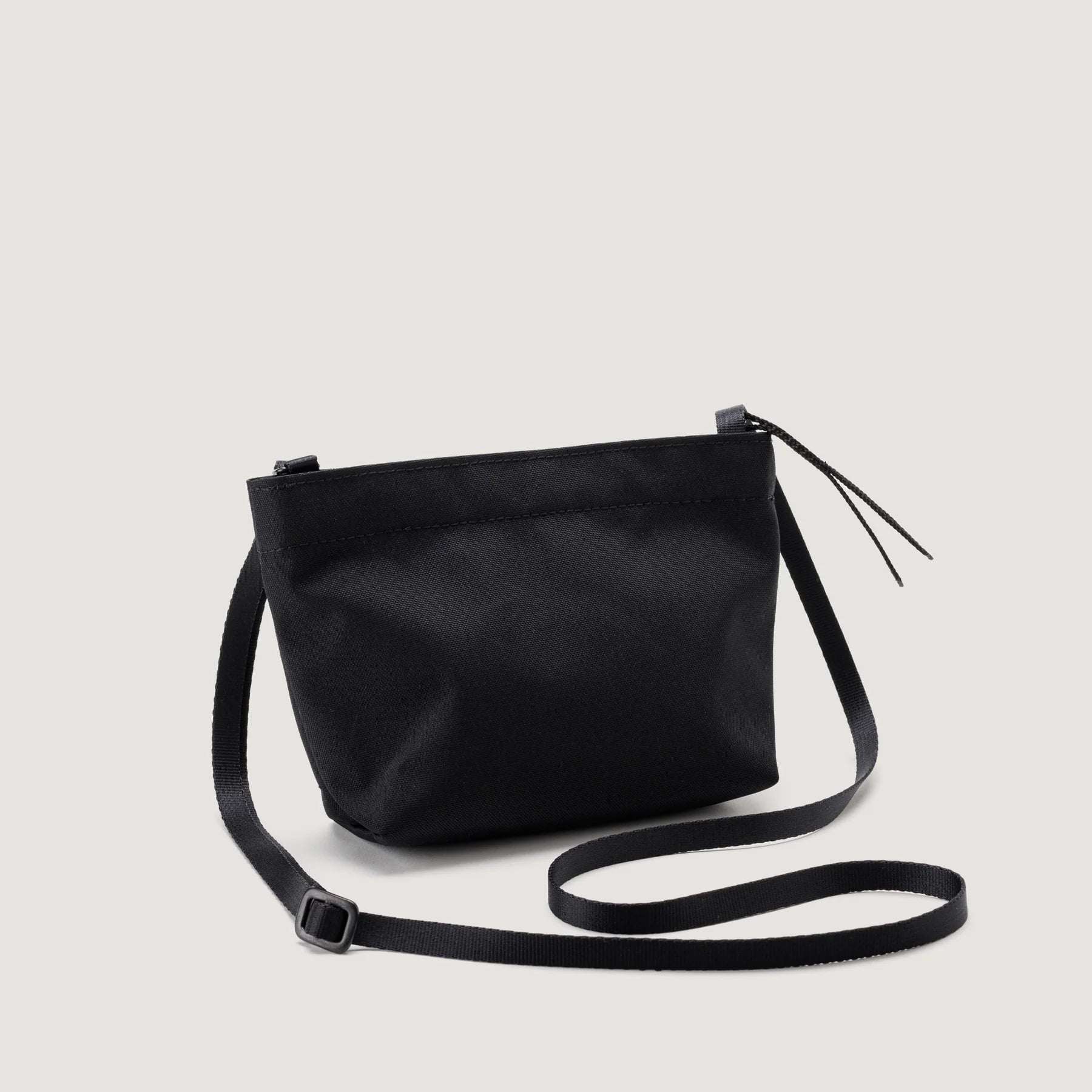 A black Zipper Pouch Mini crossbody bag with an adjustable strap and a tassel on a white background by Bags in Progress.