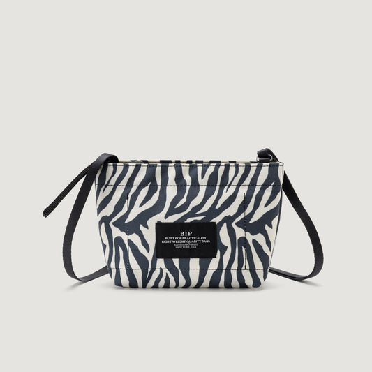 A small, Bags in Progress Zipper Pouch Mini in Zebra print with a thin black strap and a logo patch, set against a plain white background.