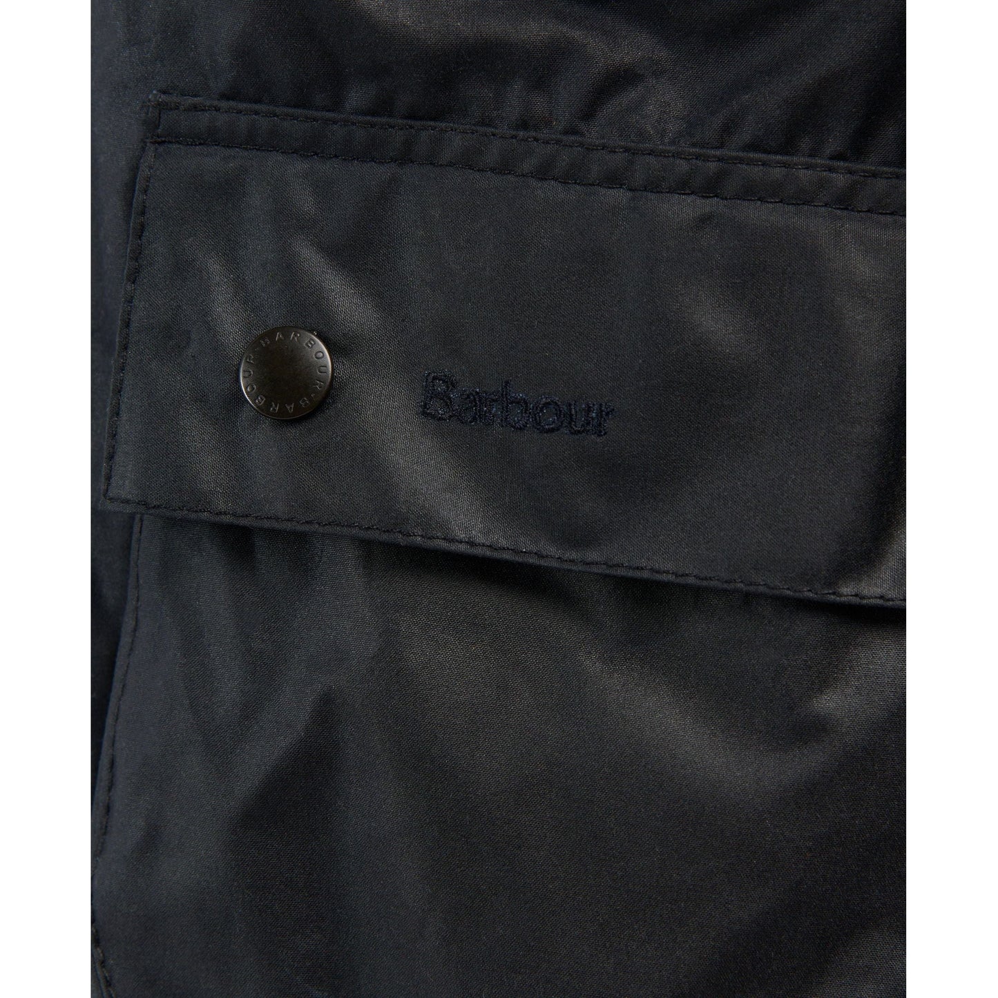 Close-up of a navy Barbour M Bedale Wax Jacket pocket with a buttoned flap, featuring the Barbour logo embroidered above the flap and complemented by a classic corduroy collar.