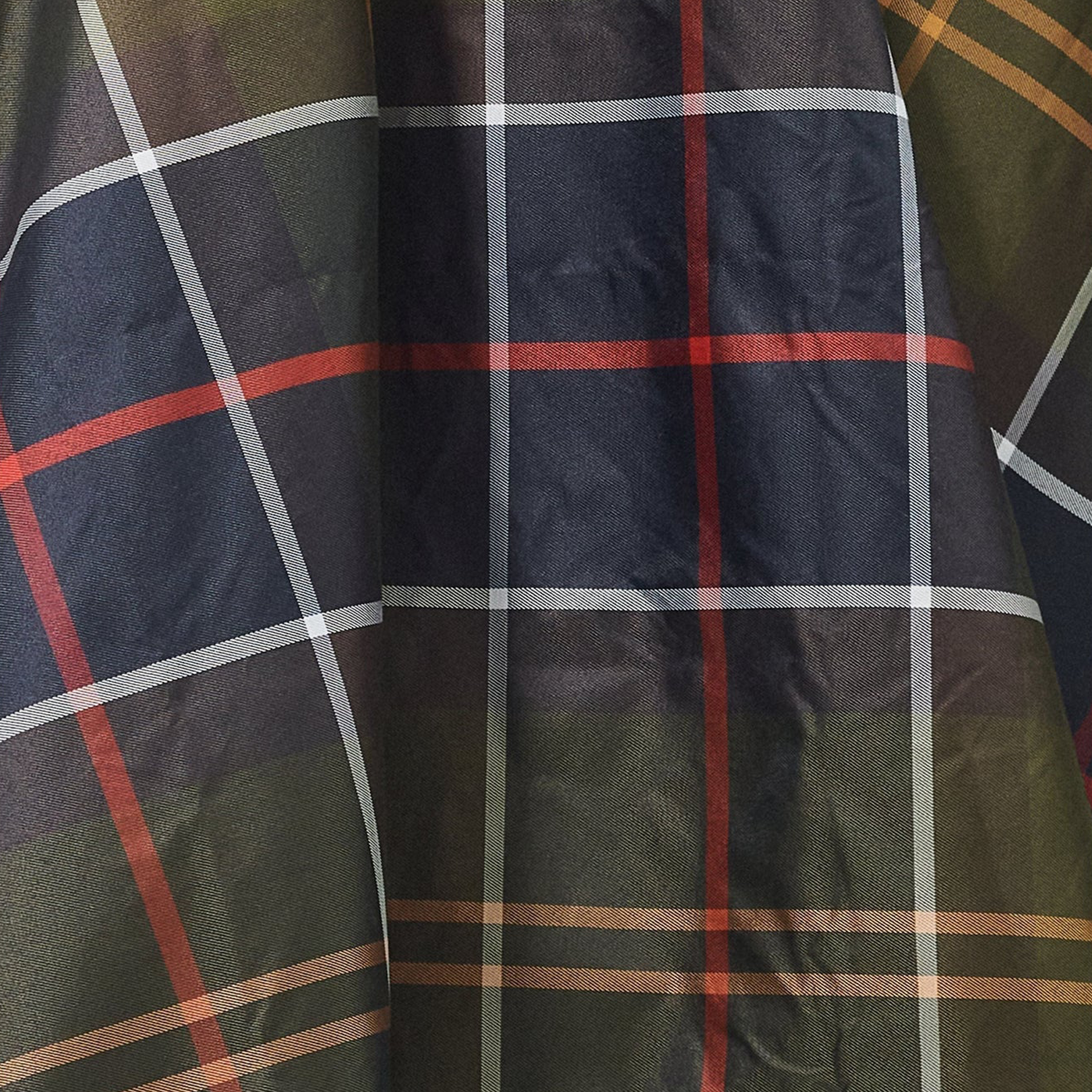 A close-up of Barbour's Tartan Showerproof Poncho showcases its dark plaid fabric, with intersecting red, white, and olive green lines.